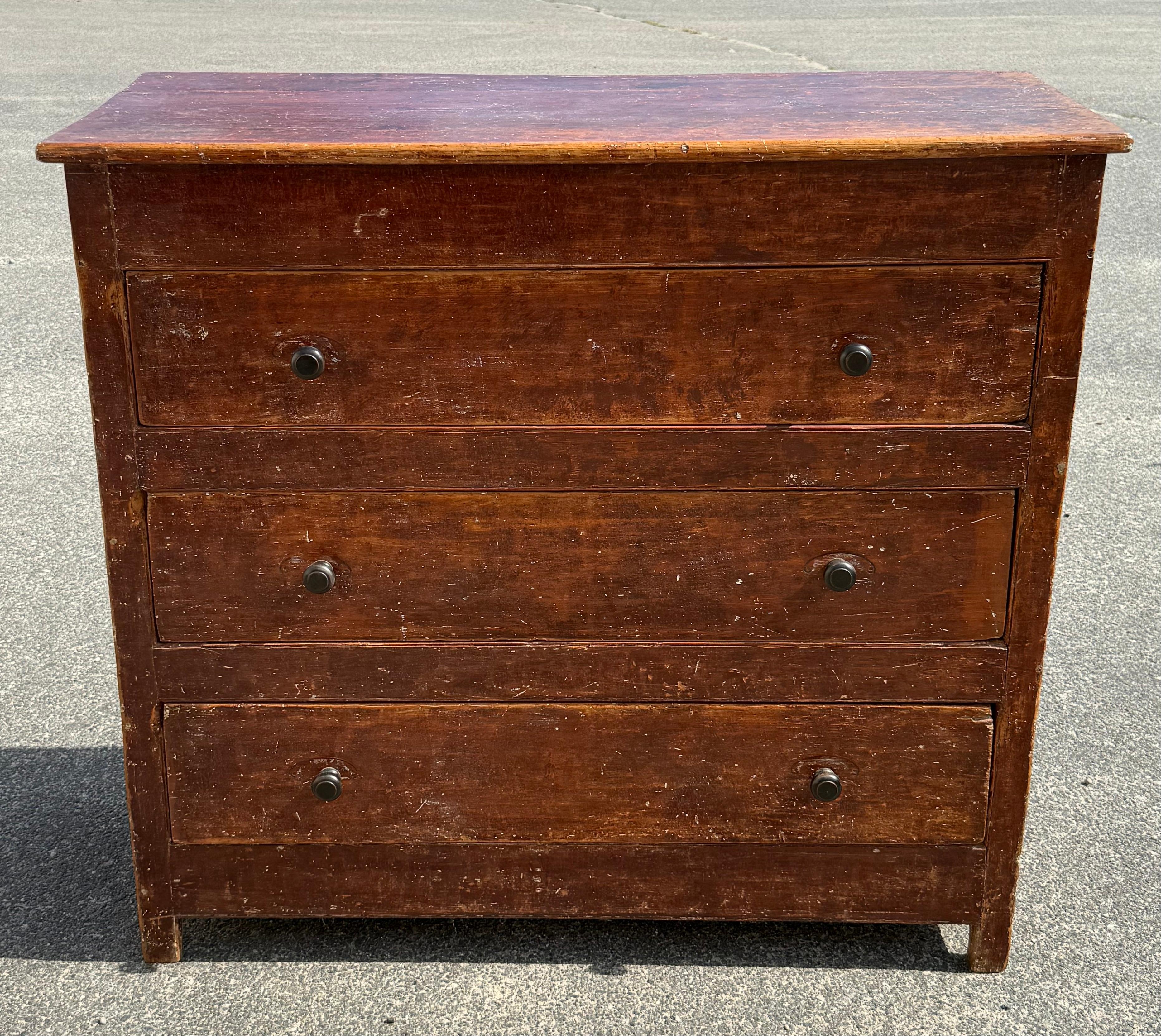 19th century pine chest of drawers in original red finish.  Tall form with three drawers and painted flourishes over the knobs.  Likely from Quebec.