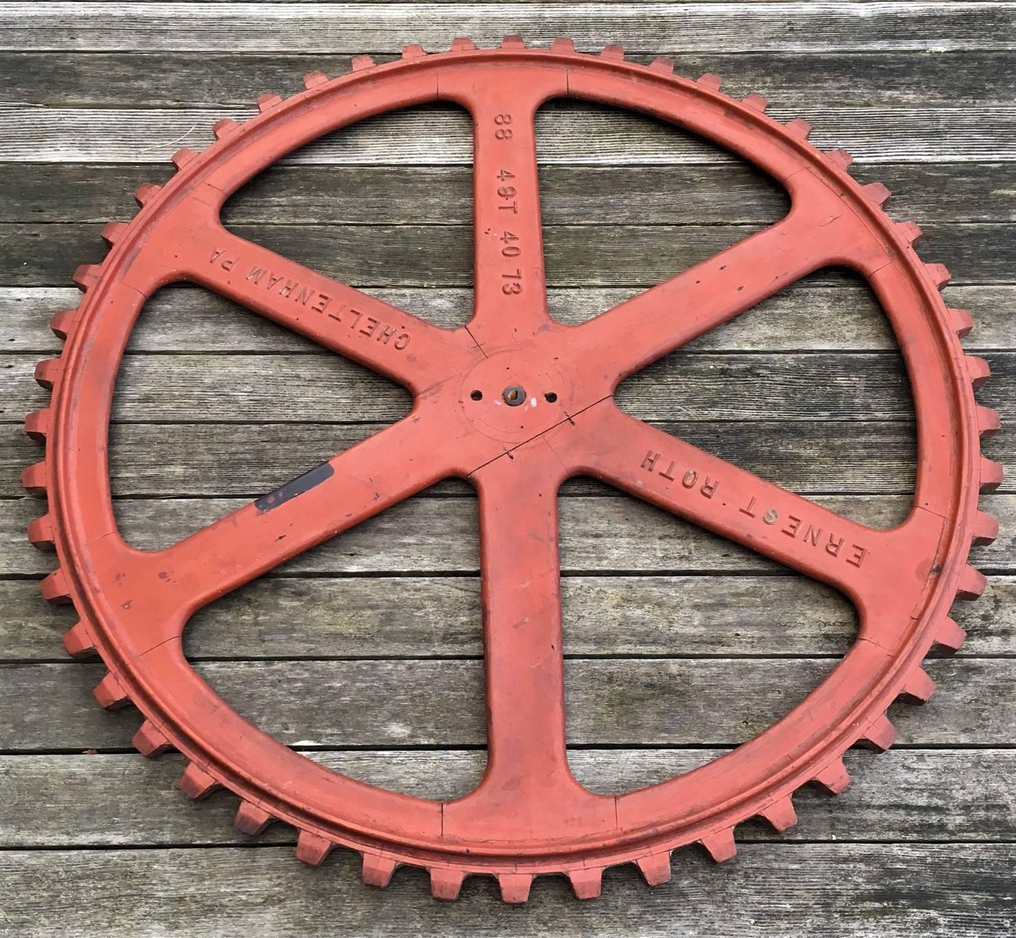 Two hand-carved wooden cog wheels, made for a foundry to cast metal cogs. They are in original red paint (the larger wheel is a darker brick red, the smaller a lighter terra cotta red). The smaller wheel has raised relief 
lettering spelling