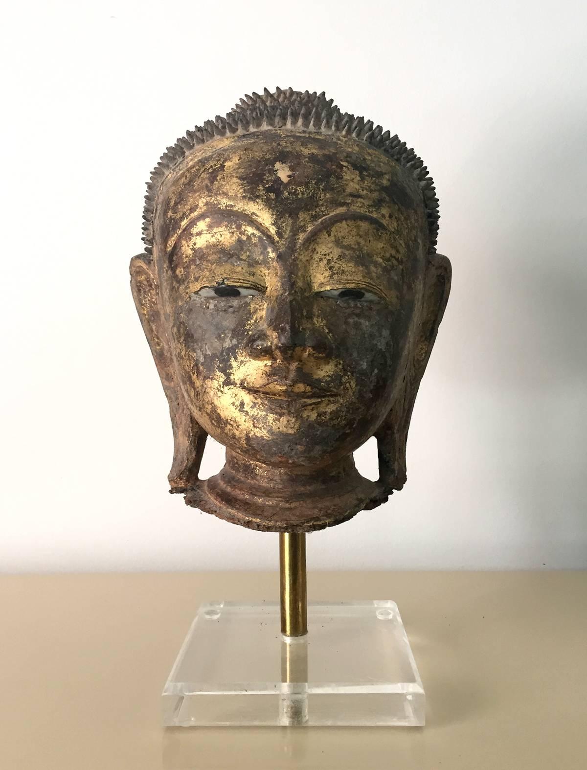 Ein vergoldeter und lackierter Holz-Buddha-Kopf, der auf einem Ständer aus Metall und Lucite ausgestellt ist. Er besticht durch seine raffinierten Merkmale und erstaunlichen Details. Die Schnitzerei ist von exquisiter Qualität. Die Augen wurden mit
