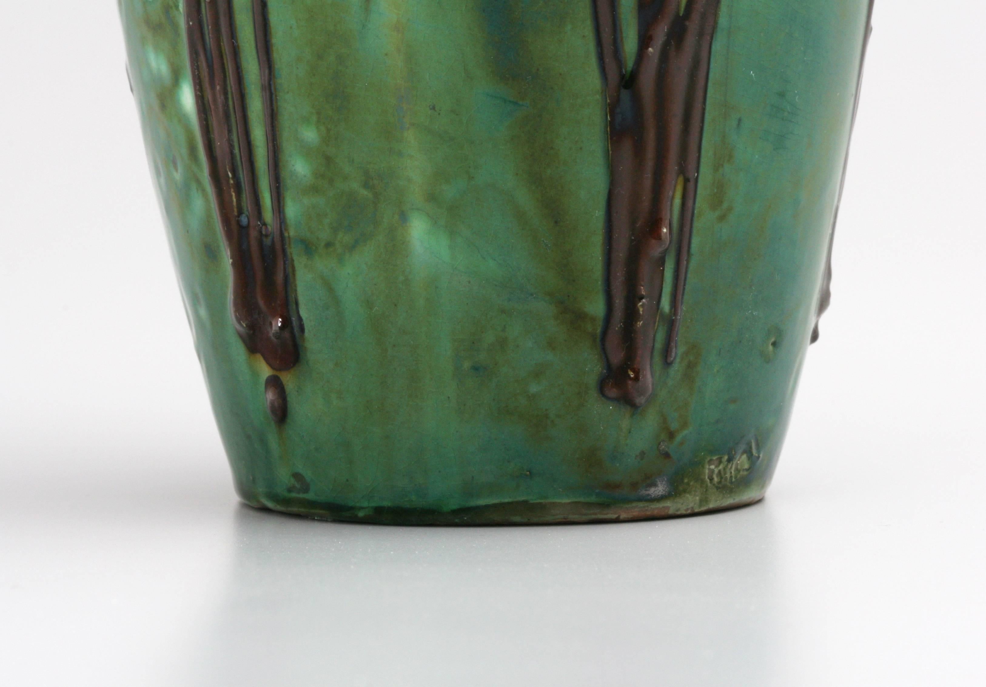 An example of lead-glazed slipware by Max Laeuger, this vibrantly colored vase depicts long-stemmed orange flowers in low relief against a background of bubbly green and inky black. Laeuger was well-known for this style in the 1890s when most of his