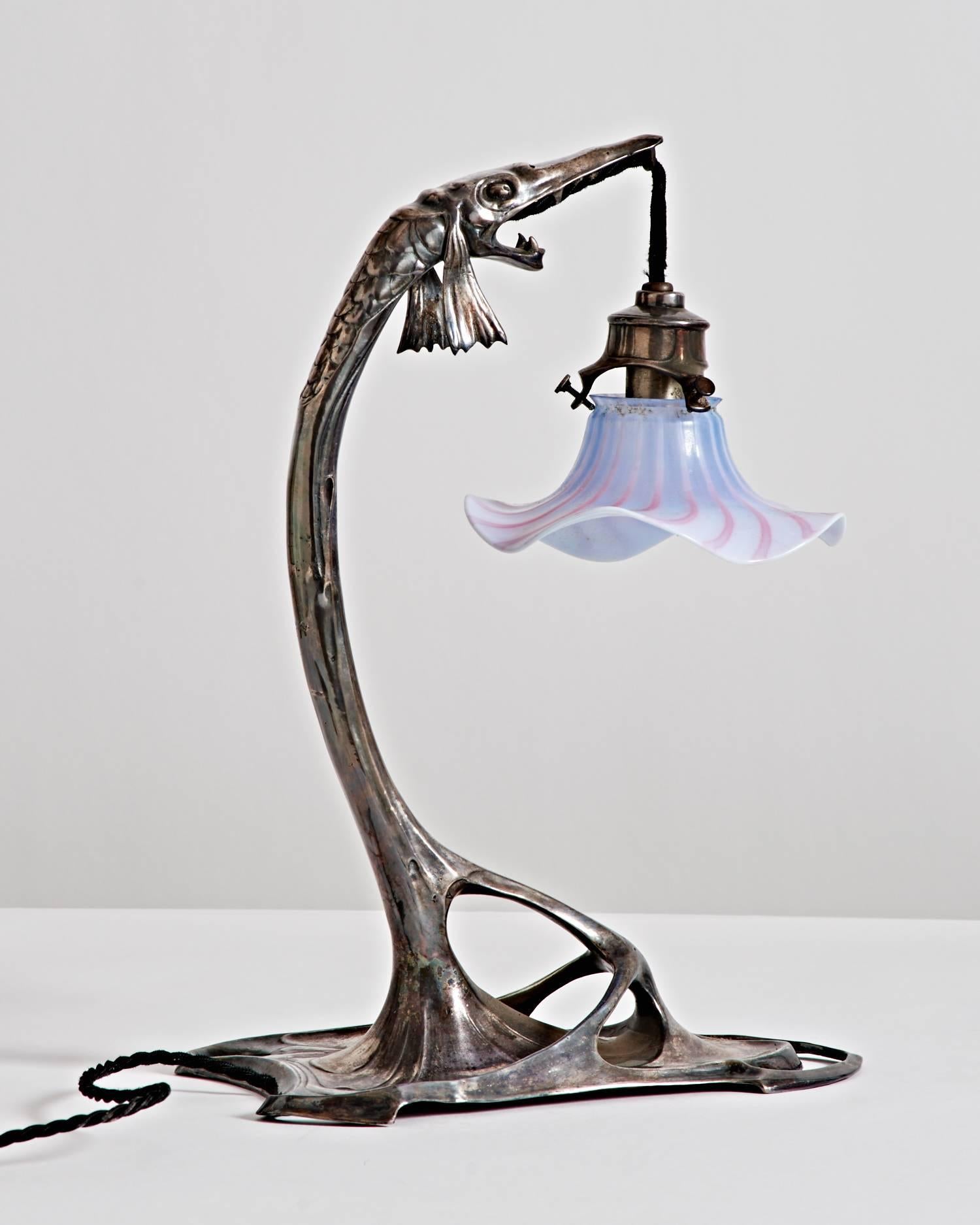 Jugendstil pewter table lamp in the form of a pike fish suspending a floriform glass shade from its mouth.