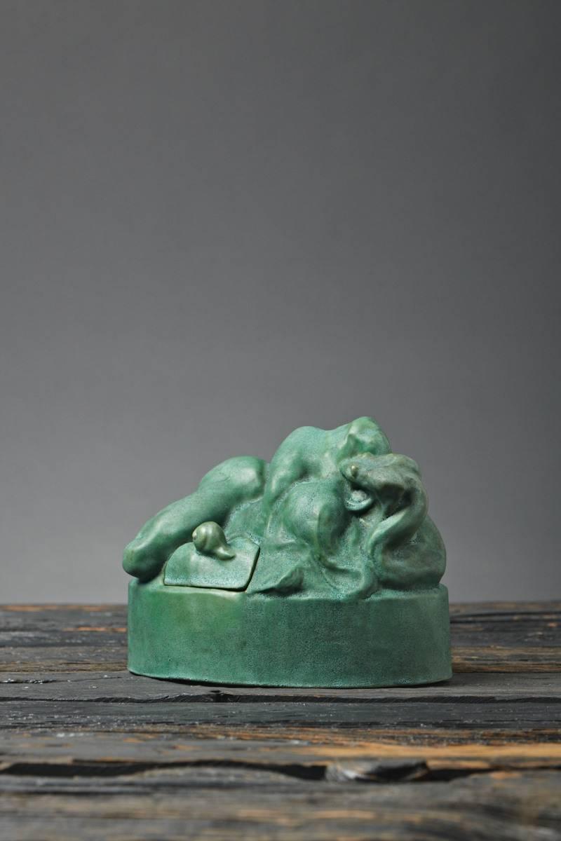 A remarkable and possibly unique sculpture depicting a recumbent woman constricted by a python, whose tail penetrates her in an act of anal intercourse. The piece may also have served as a box or inkwell, as evidenced by the snail-knobbed lid on one