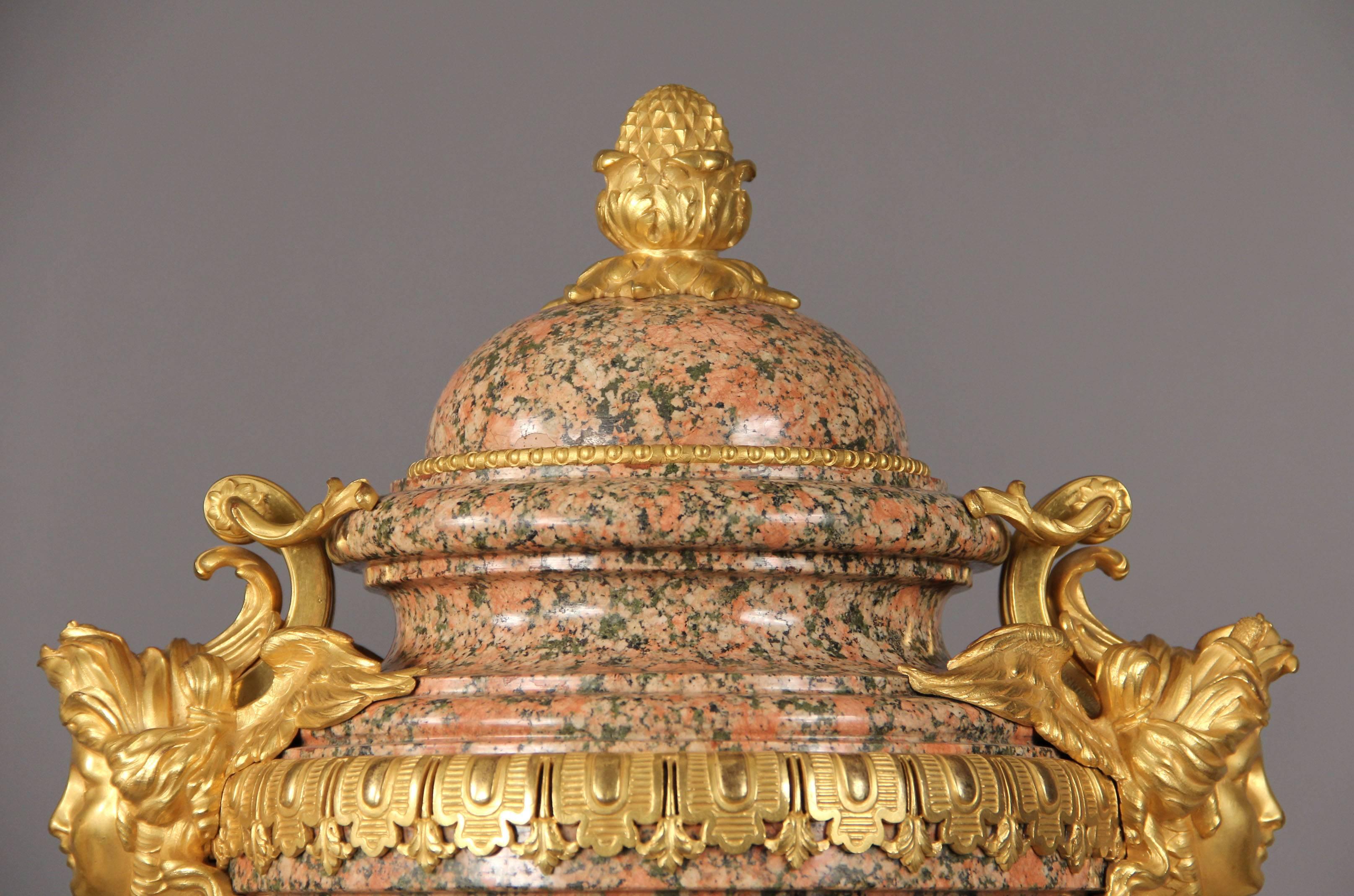 A rare pair of late 19th-early 20th century french bronze-mounted pink granite urns.

Each domed lid with pinecone finial, each side with winged female mask, on paw-footed supports and shaped plinth.
 