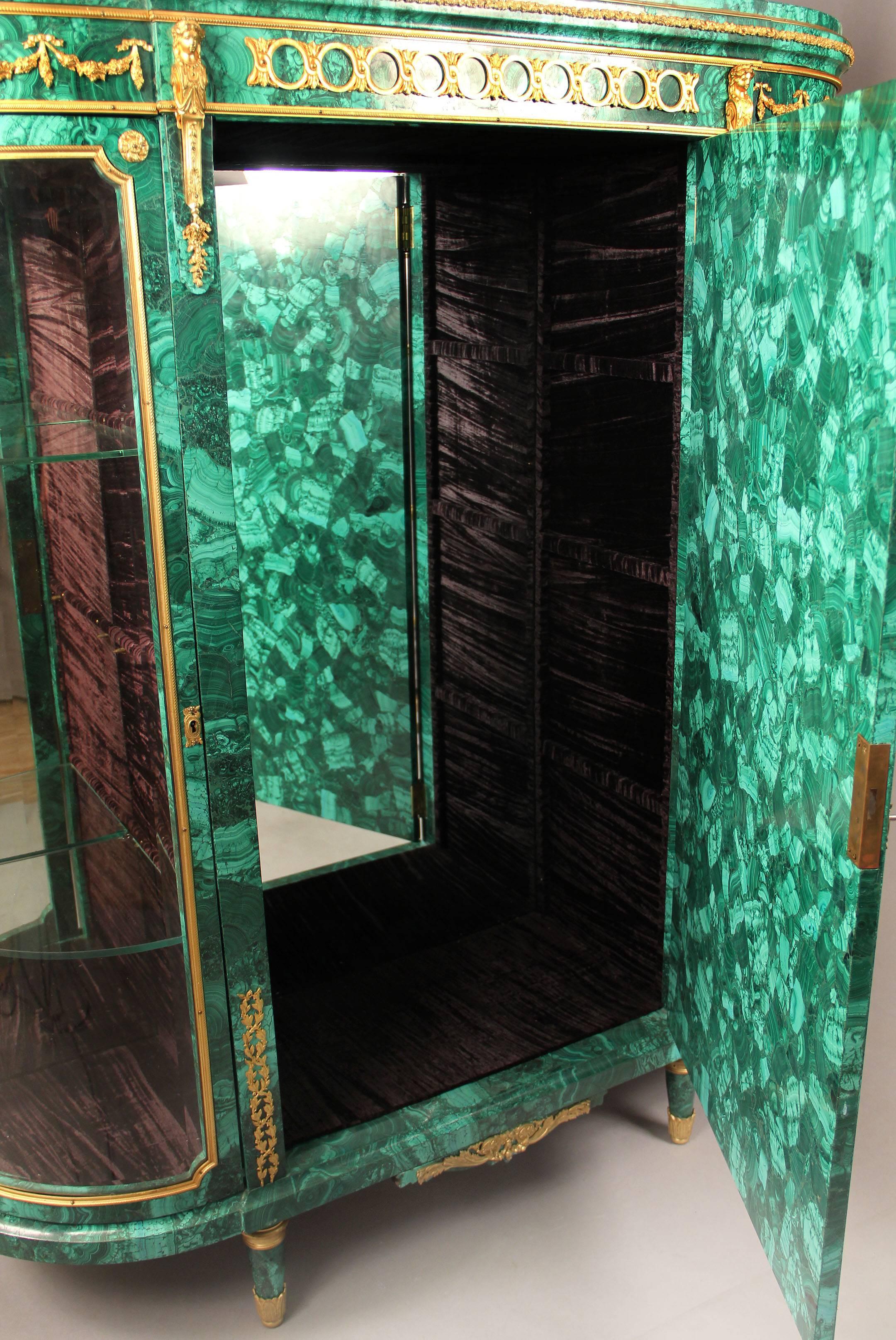 A very fine early 20th century gilt bronze-mounted Louis XVI style Malachite Vitrine cabinet

The D-shaped top over central cupboard door flanked by two glazed cavetto doors opening to glass shelves, raised on short tapering legs, the central door