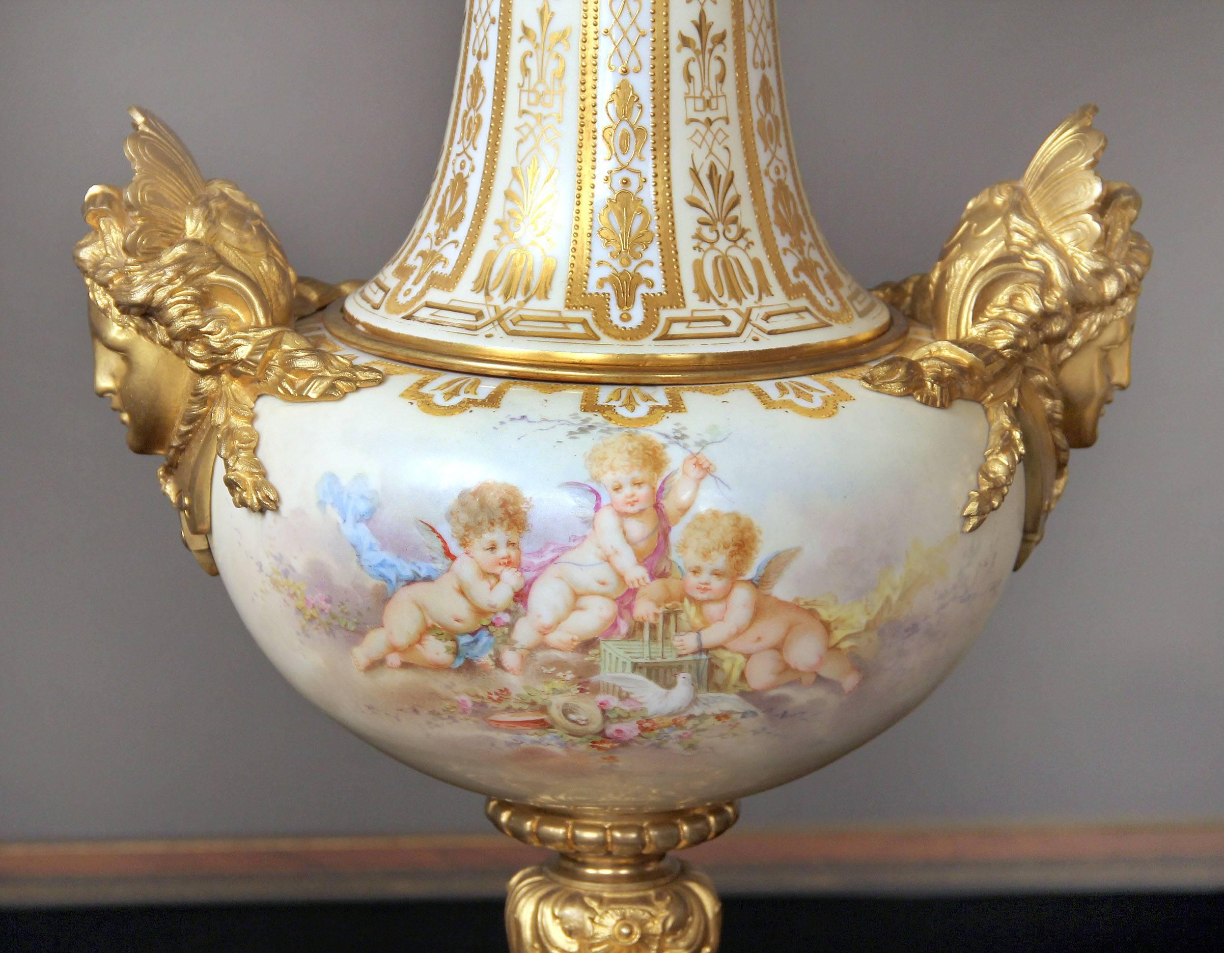 A beautiful pair of late 19th century gilt bronze and champlevé enamel mounted white Sèvres style vases

Gilt bronze tops above a long neck with raised gold designs. The painted fronts each with scenes of cherubs, flowers, birds and fruit, the