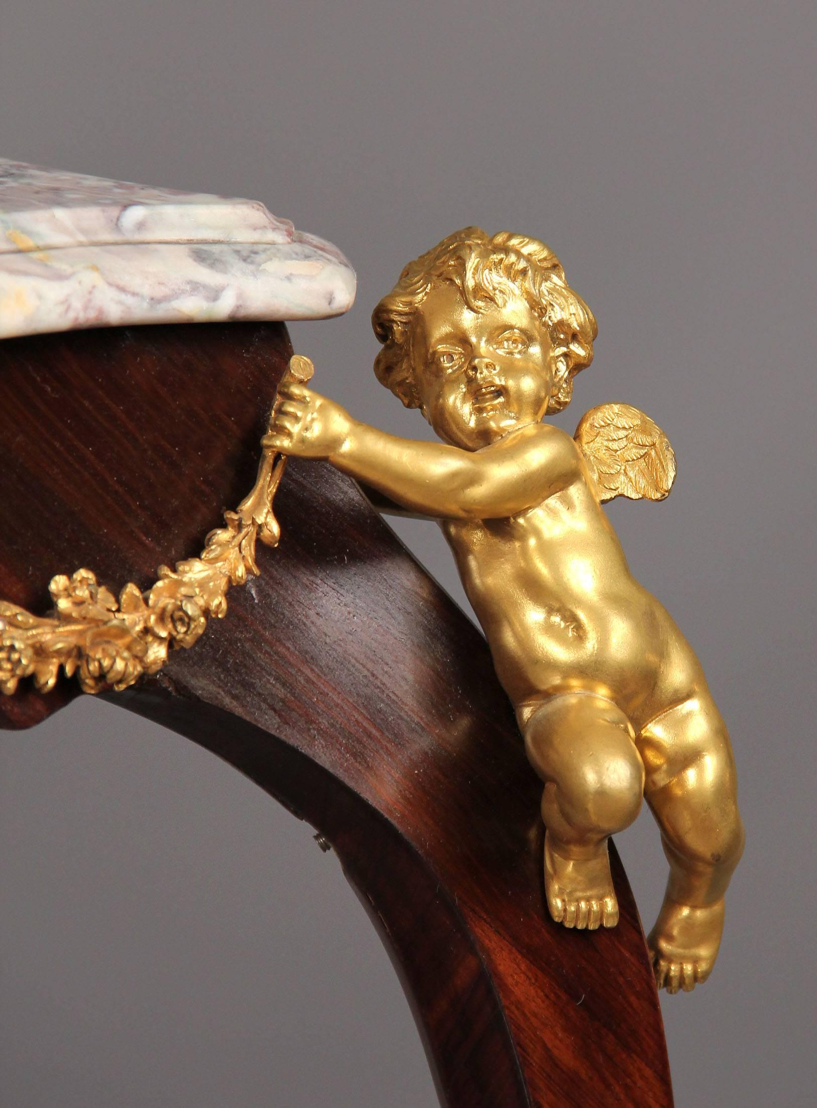 A beautiful late 19th century Louis XV style gilt bronze-mounted kingwood tea table with cherubs.

By Theodore Millet.

Each section with a molded breche Violette marble-top, each corner with a putti holding flower swags, the table with scrolled