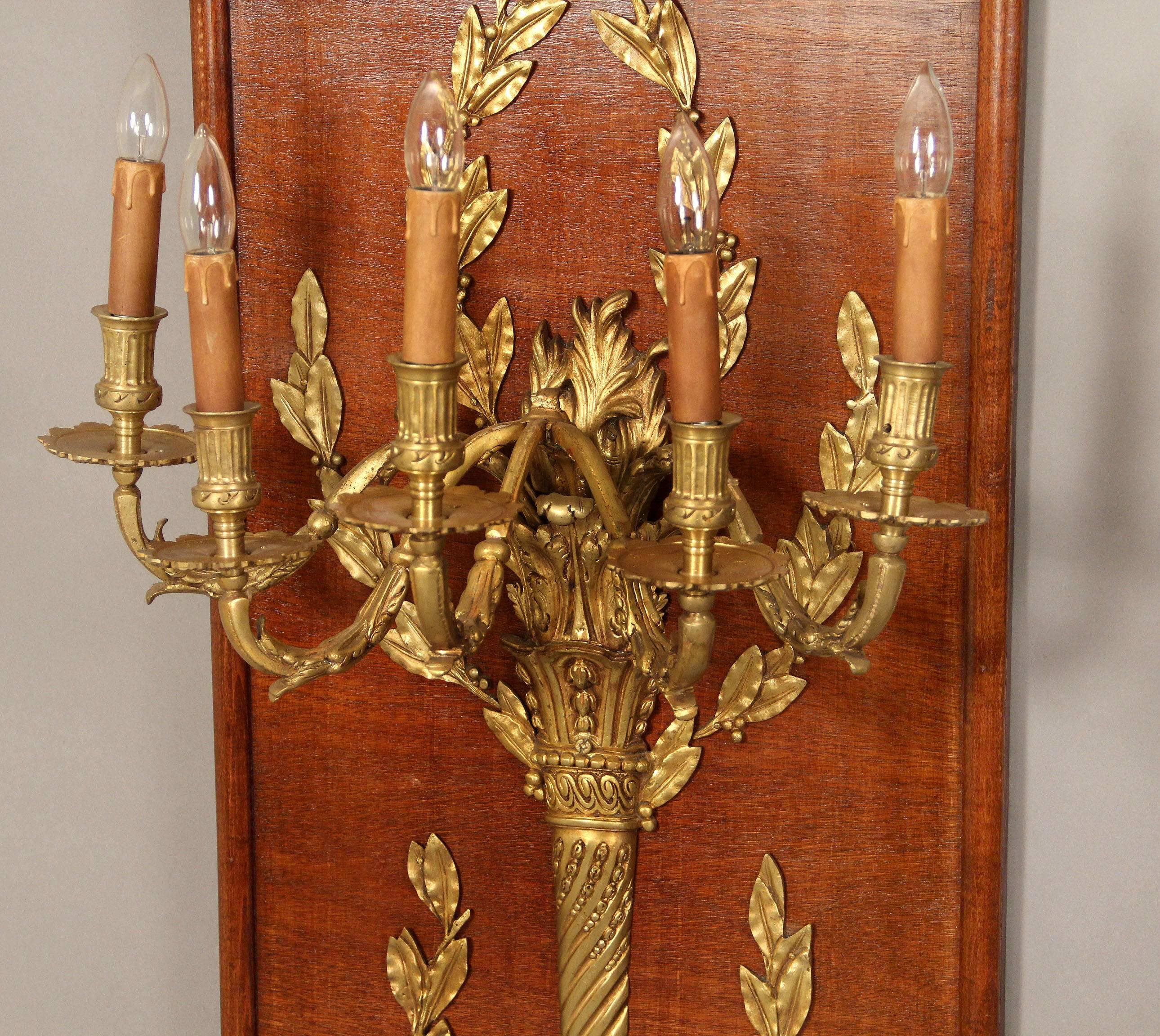 A wonderful and large set of four 20th century gilt bronze mounted five light sconces.

Each mounted on a rectangular mahogany panel, bronze foliage designs centered by a torch.