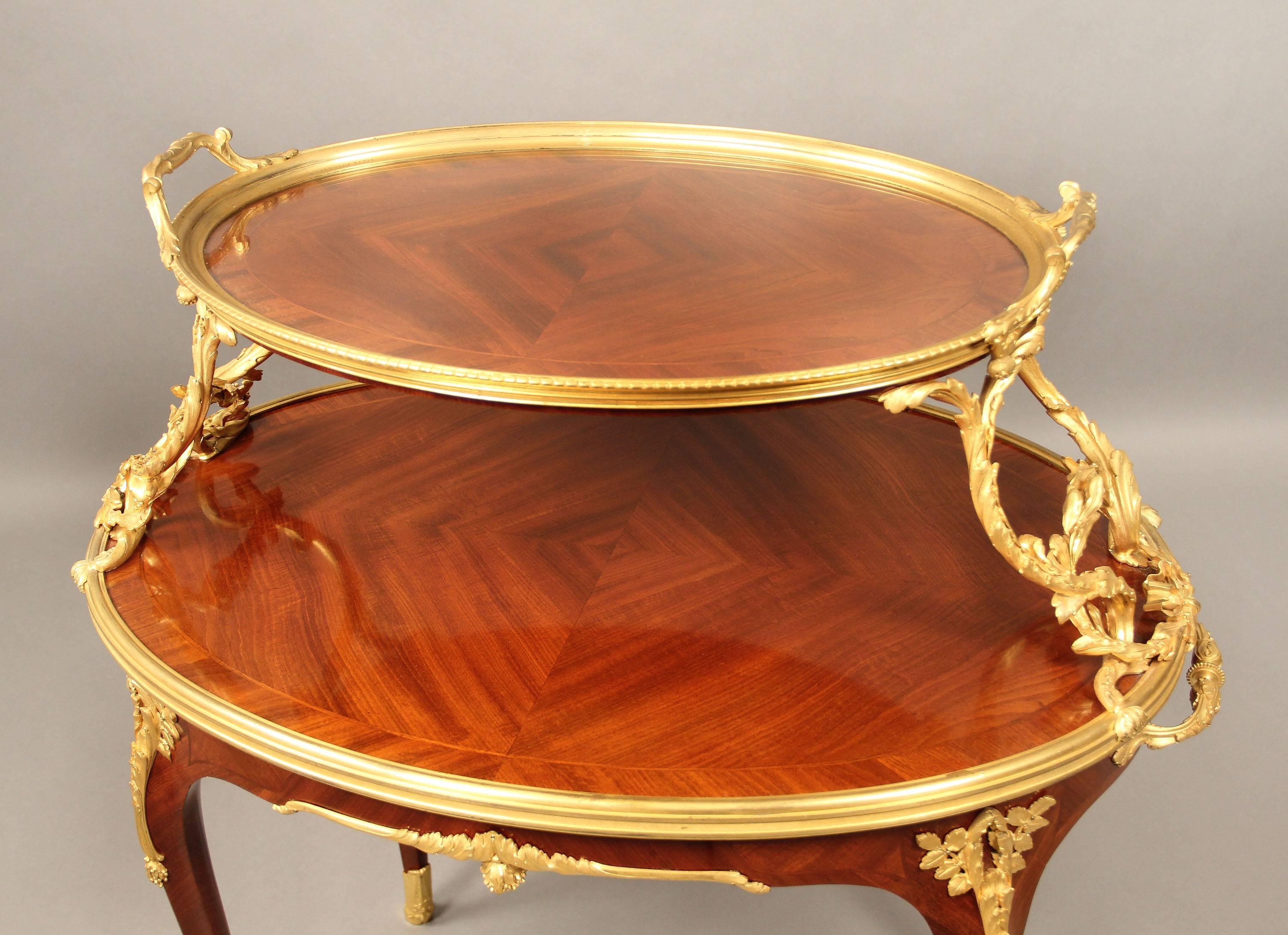 A fine late 19th century gilt bronze-mounted Louis XV style two-tier tea table.

By Paul Sormani.

The oval upper tier surmounted by an bronze framed removable glass tray held to each side by a scrolled berry hung vine and laurel garland