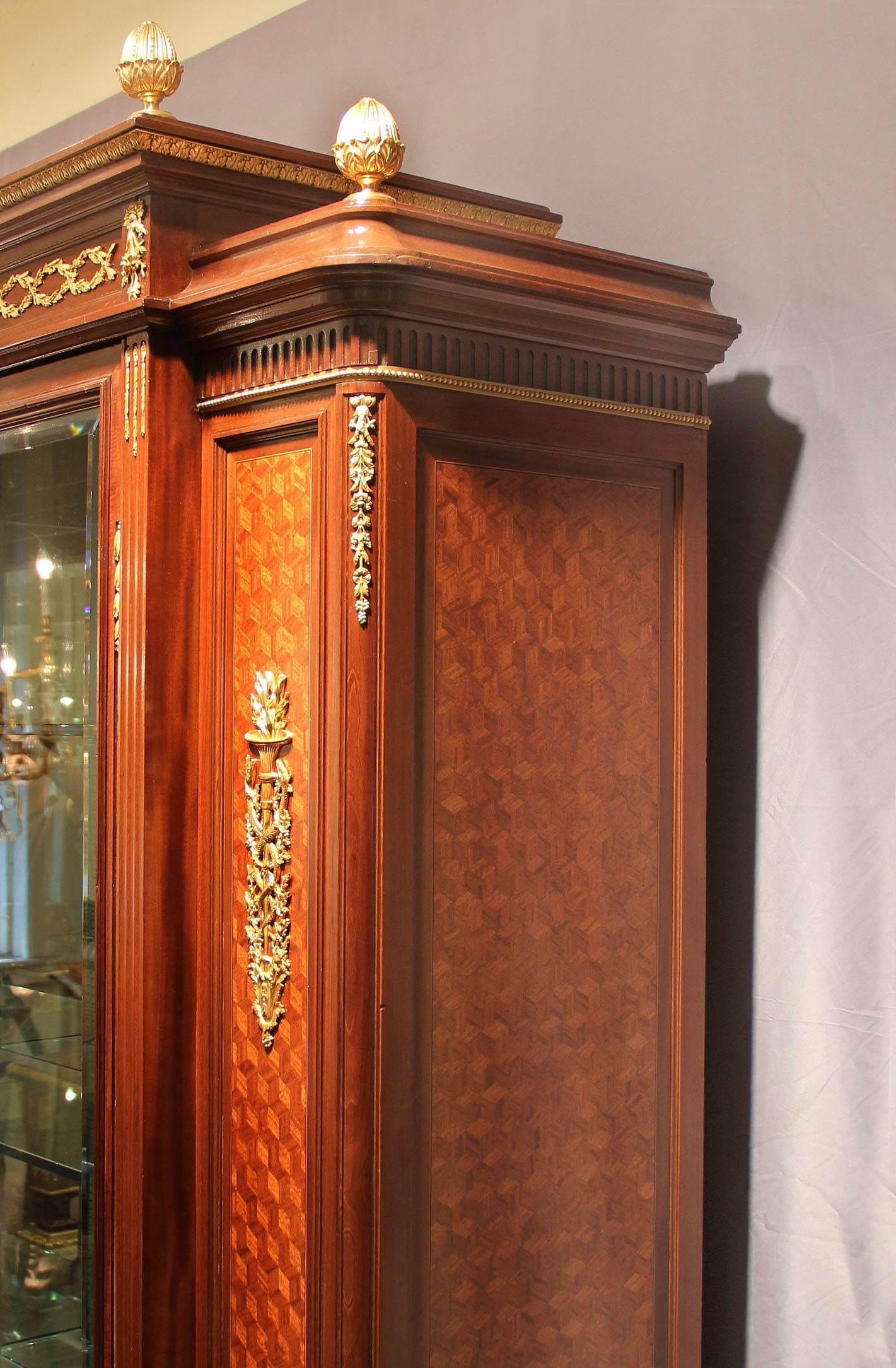 An large and fine early 20th century Louis XVI style gilt bronze-mounted parquetry vitrine

by François Linke.

A single center door flanked by parquetry sides with bronze mounted designs of serpents and torches, the top with a bronze frieze