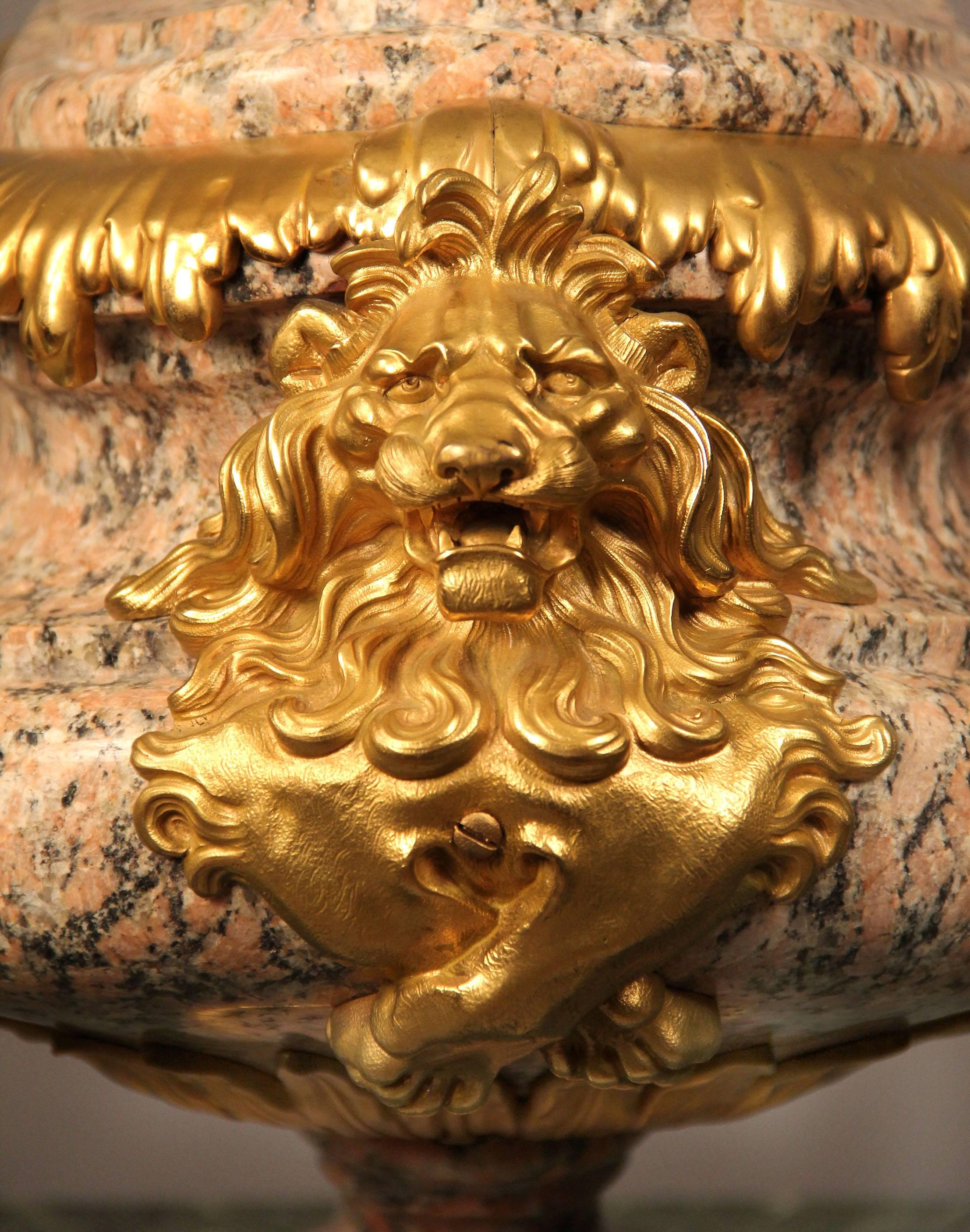 Un raffinato centrotavola francese della fine del XIX secolo in granito rosa e bronzo dorato,

di forma ovale, i lati con maschere di leone e la parte superiore incurvata sormontata da una bacca e da un acanto.
