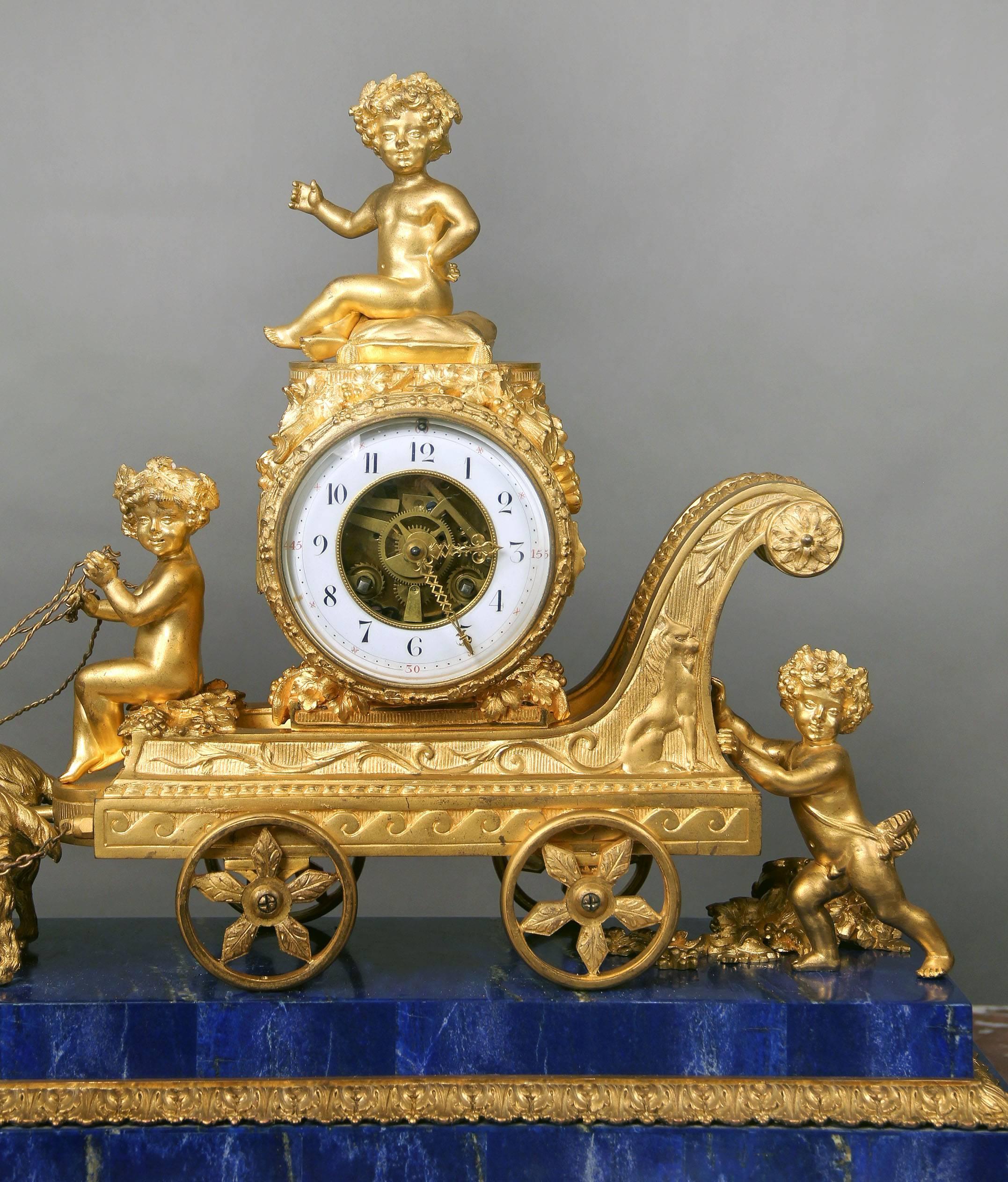 A rare and great quality late 19th century gilt bronze and lapis lazuli mantel clock. 

The bronze clock shaped as a cart surrounded by three putti, being pulled by two ram's. Raised on a lapis veneered rectangular base. The twin train movement