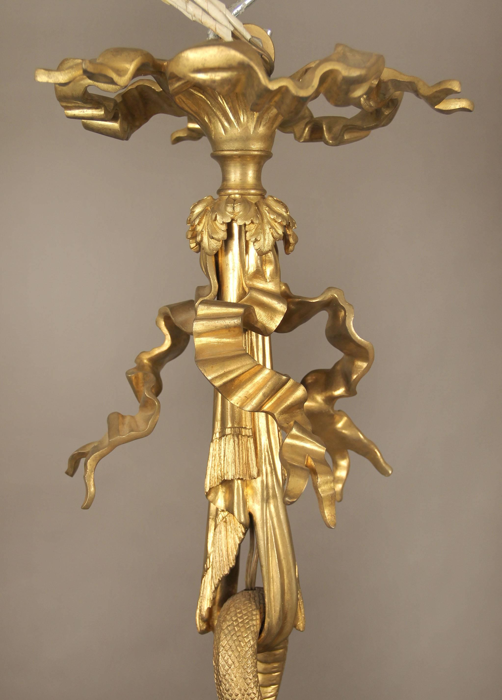 A stunning and important late 19th century gilt bronze fifteen-light chandelier.

By Maison Millet.

A central lyre shaped stem with satyrs masks, suspended by a serpent and a flower garland, the top as a bow and the base with instruments.