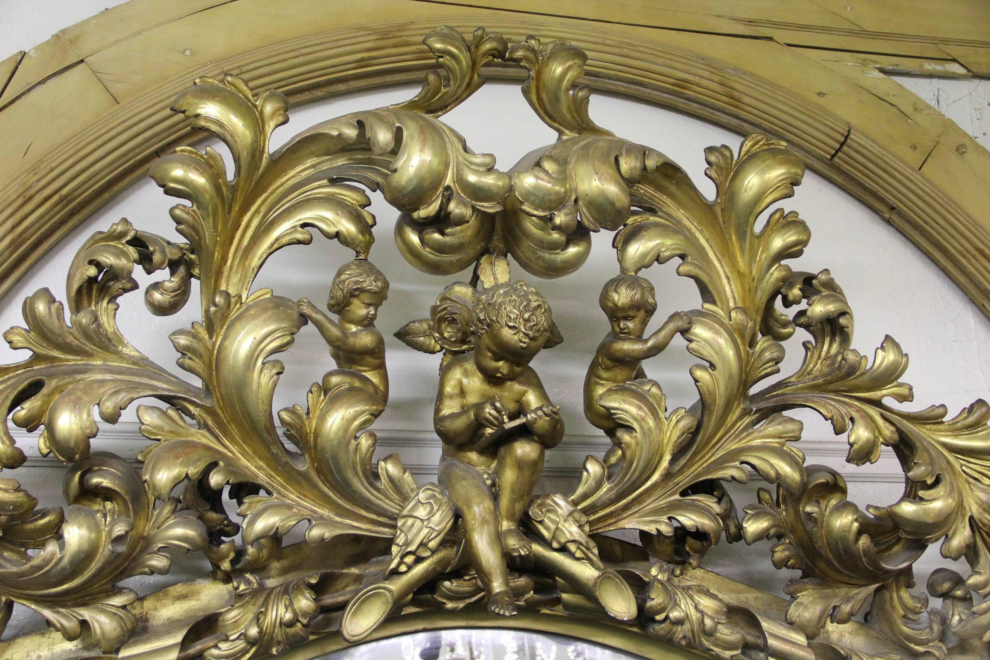 A very important late 19th century Rococo style giltwood and gesso mirror.

The entire frame exceptionally carved with heavy detail. The top centered with a large carved cherub and two putti surrounded by flowers and foliage.