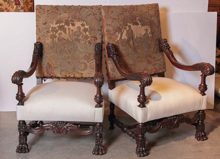 This wonderful pair of antique walnut wood armchairs has the original needlepoint and petit point on their high chair backs. They feauture mythological scenes at the center surrounded by foliate and floral motifs.  This is affixed to the frame with