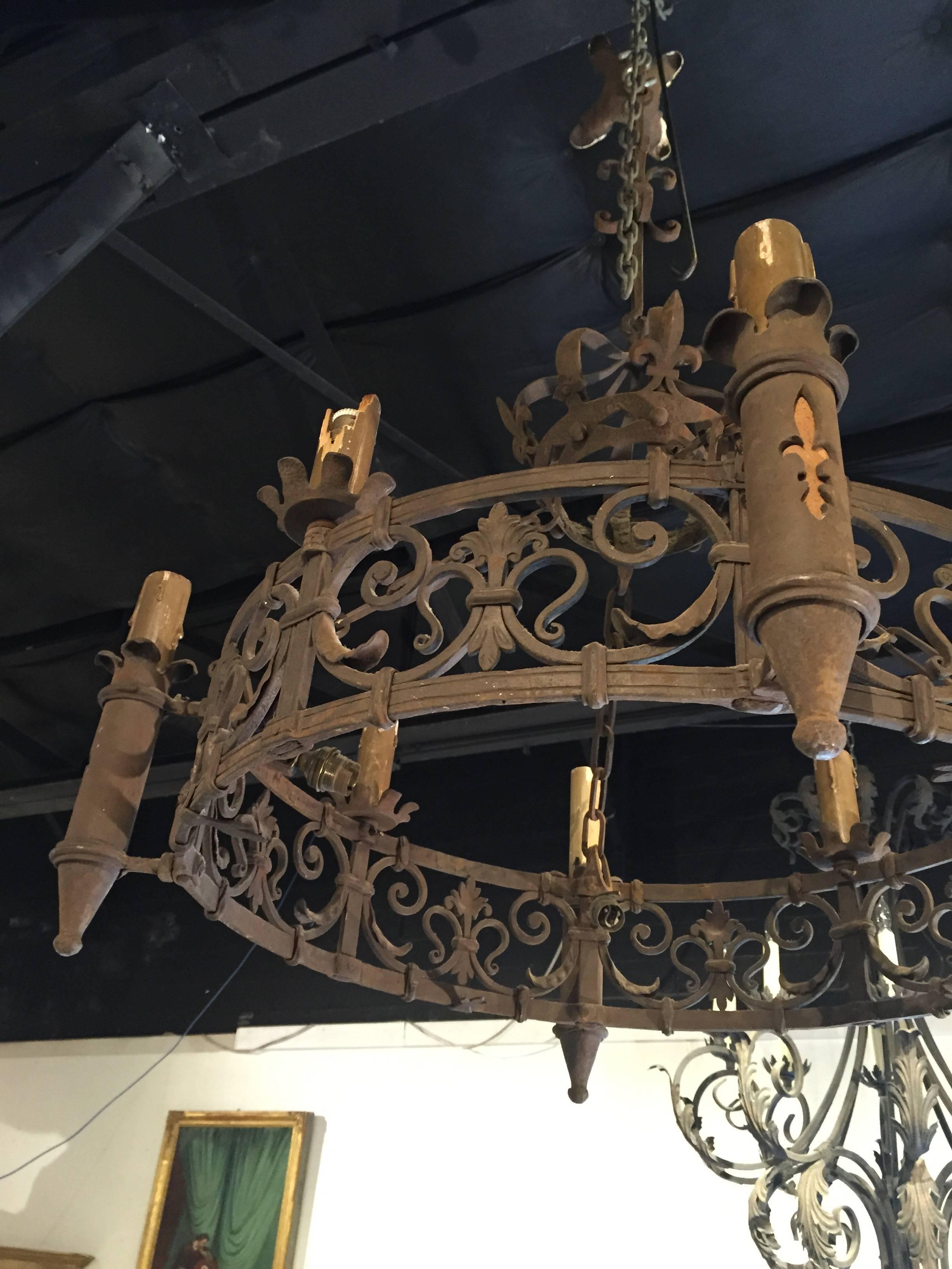 The variety of stylized fleur de lys on this circular, forged iron chandelier from France displays the artistry of its designer. The canopy is an open worked stylized crown, interspersed with fleur de lys around the banded area.  The tall circular