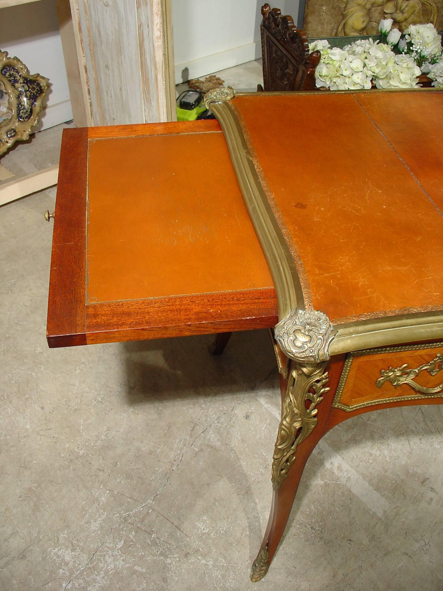This elegant Louis XV Style bureau plat or rectangular wood writing desk has an embossed leather paneled top with ormolu motifs and moldings.  There are three drawers with the center drawer being recessed and the flanking drawers flush with the