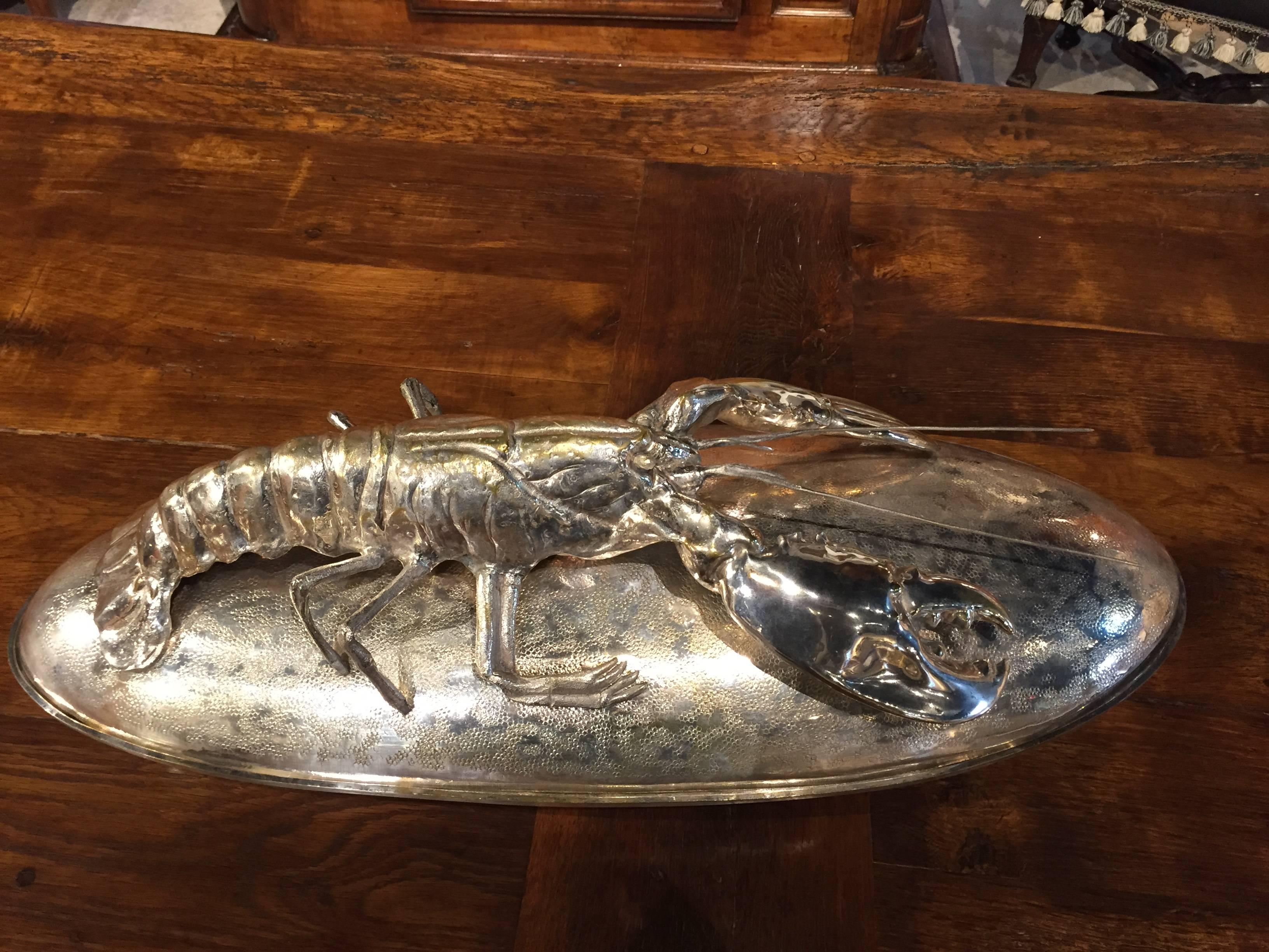 This large and beautiful lobster platter or presentation dish is silver plated over brass. A life sized lobster rests atop a hammered lid replicating scales. The artist’s rendition of the lobster is superb. There are marks to the bottom, by the