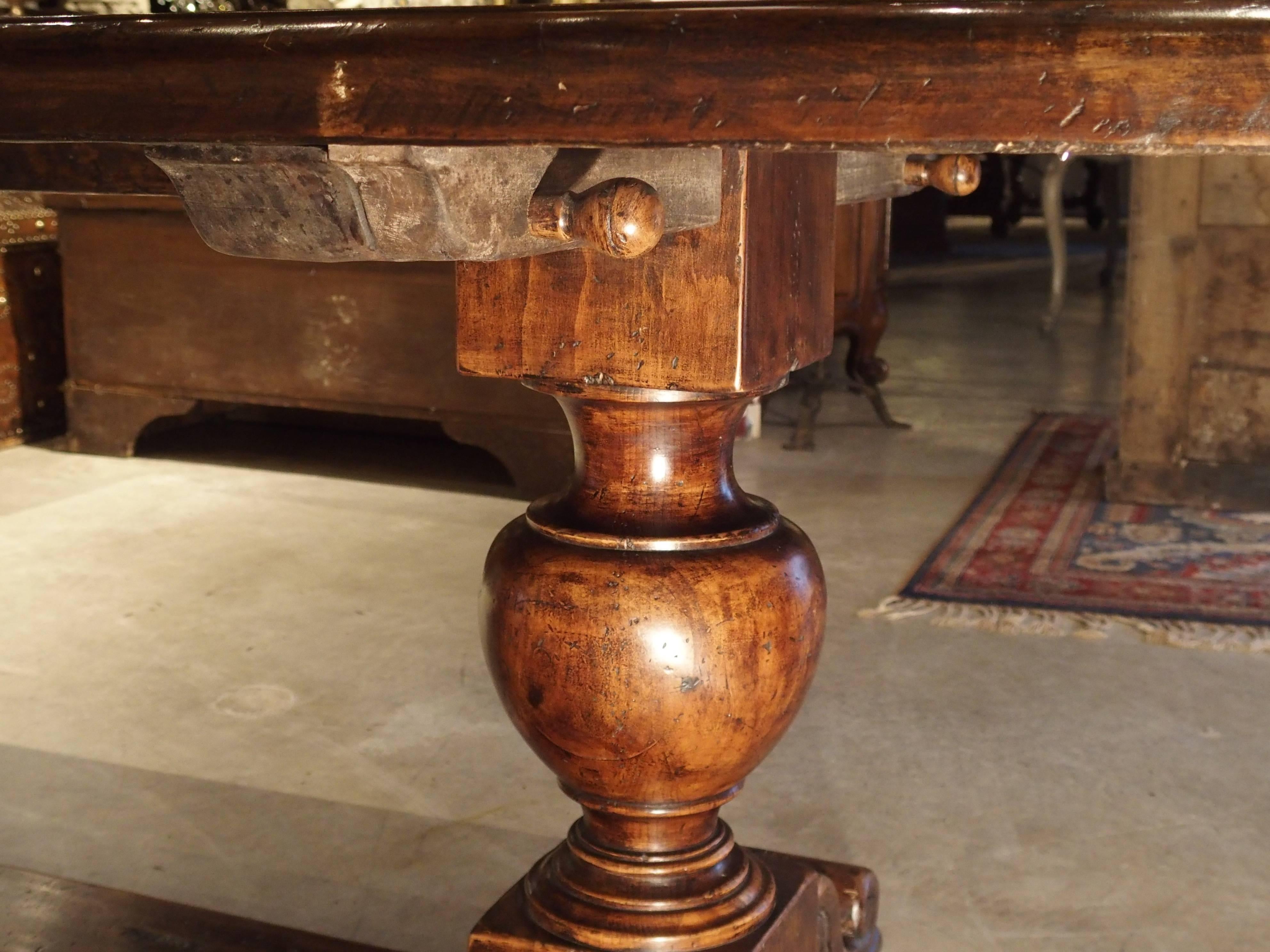 This stunning and long Italian table has been made from walnut wood. It has three round baluster shaped legs with volute feet on either end and at the center. We believe the legs to be more recent, while the top is made from salvaged wood. Under the