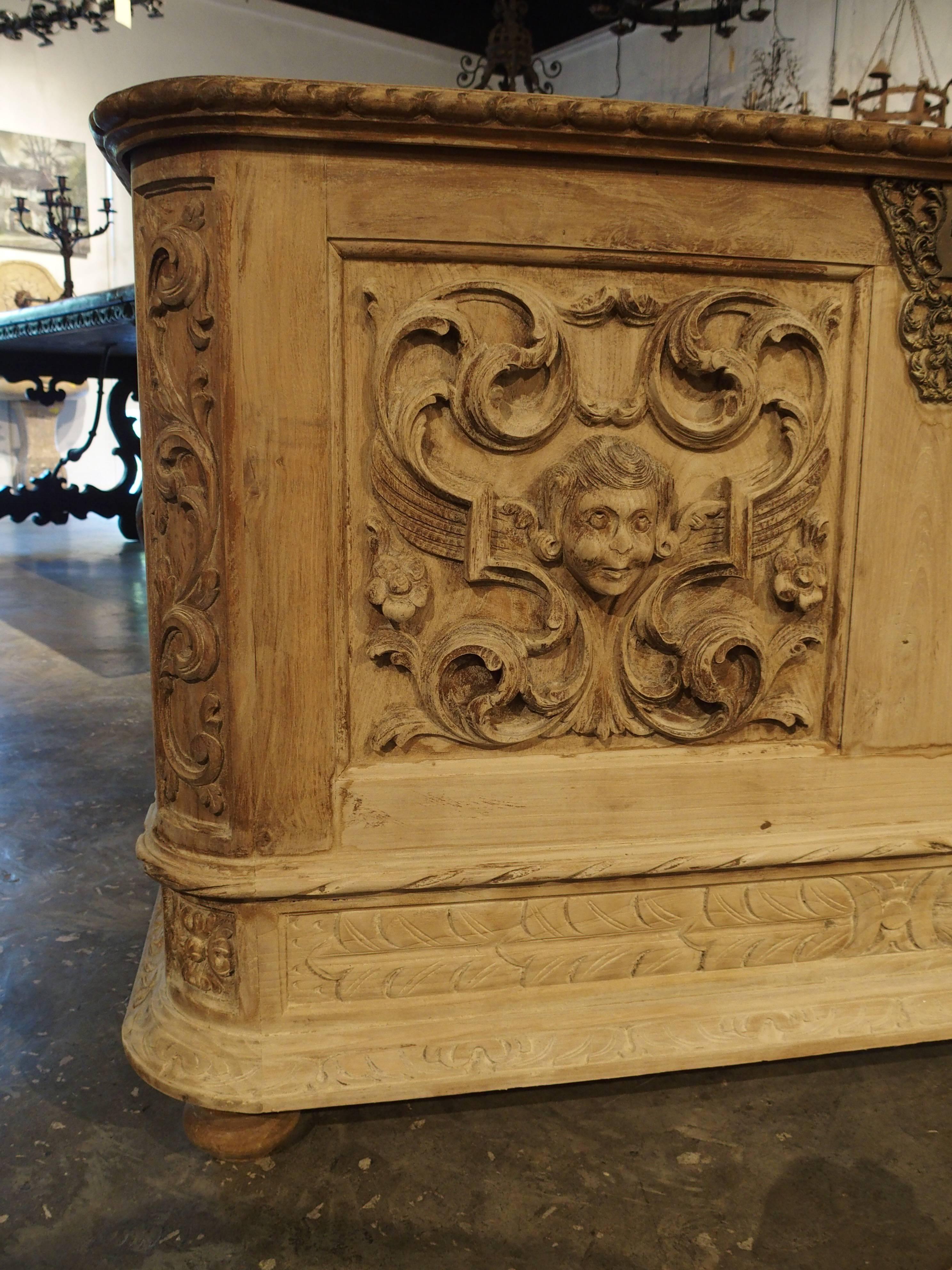 This attractive Italian trunk has highly carved motifs on three sides and has been recently stripped/cleaned.  The front has two panels with scrolling acanthus leaves with florets surrounding a carved face. There is an intricately cast lock (no key)