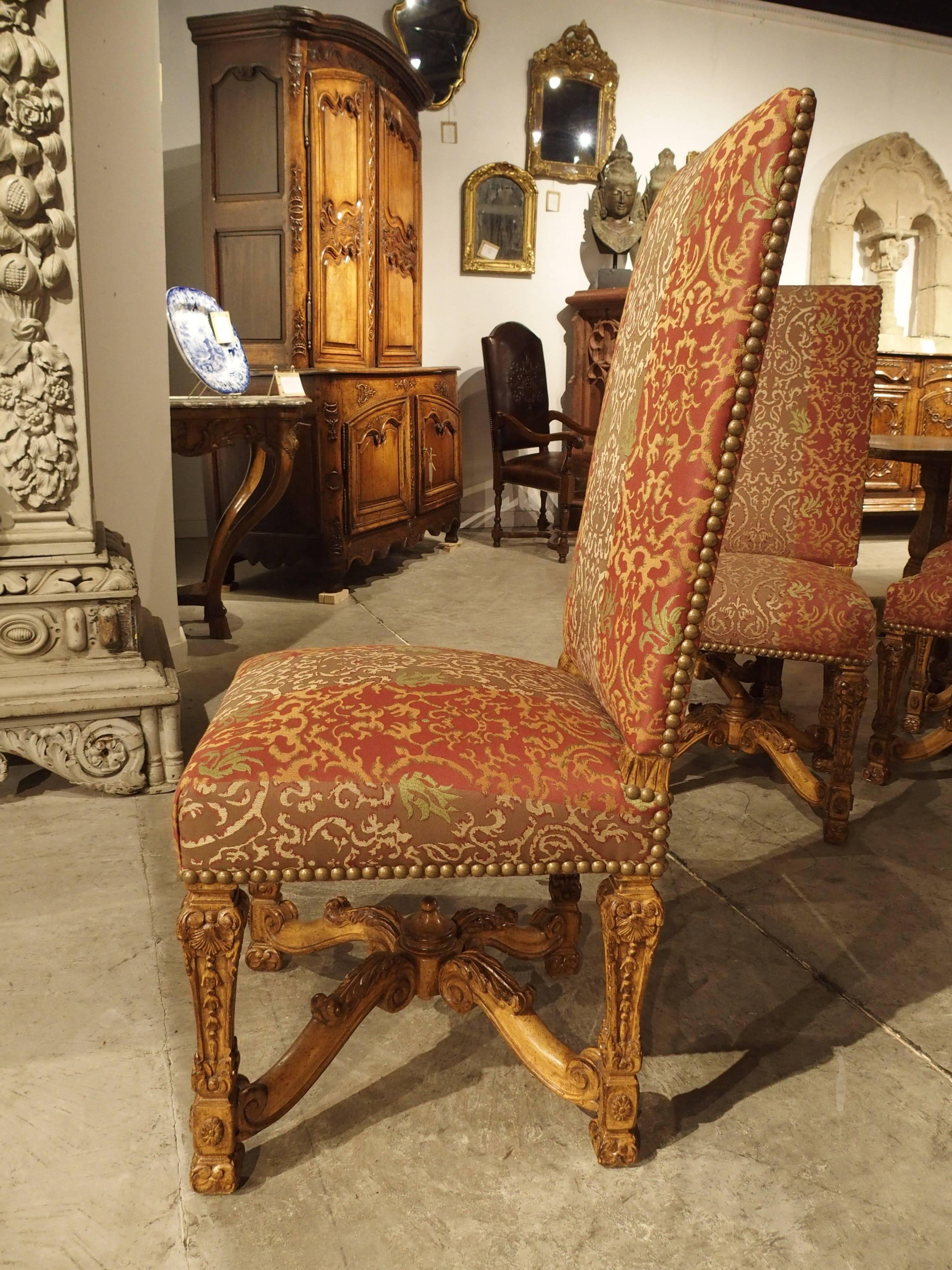 This majestic set of 12 Louis XIV style chairs date to the 1900s. There are ten side chairs and two fauteuils or armchairs. They have been upholstered with brass nailheads in an elegant damask fabric complementing the chairs’ style. All of the wood