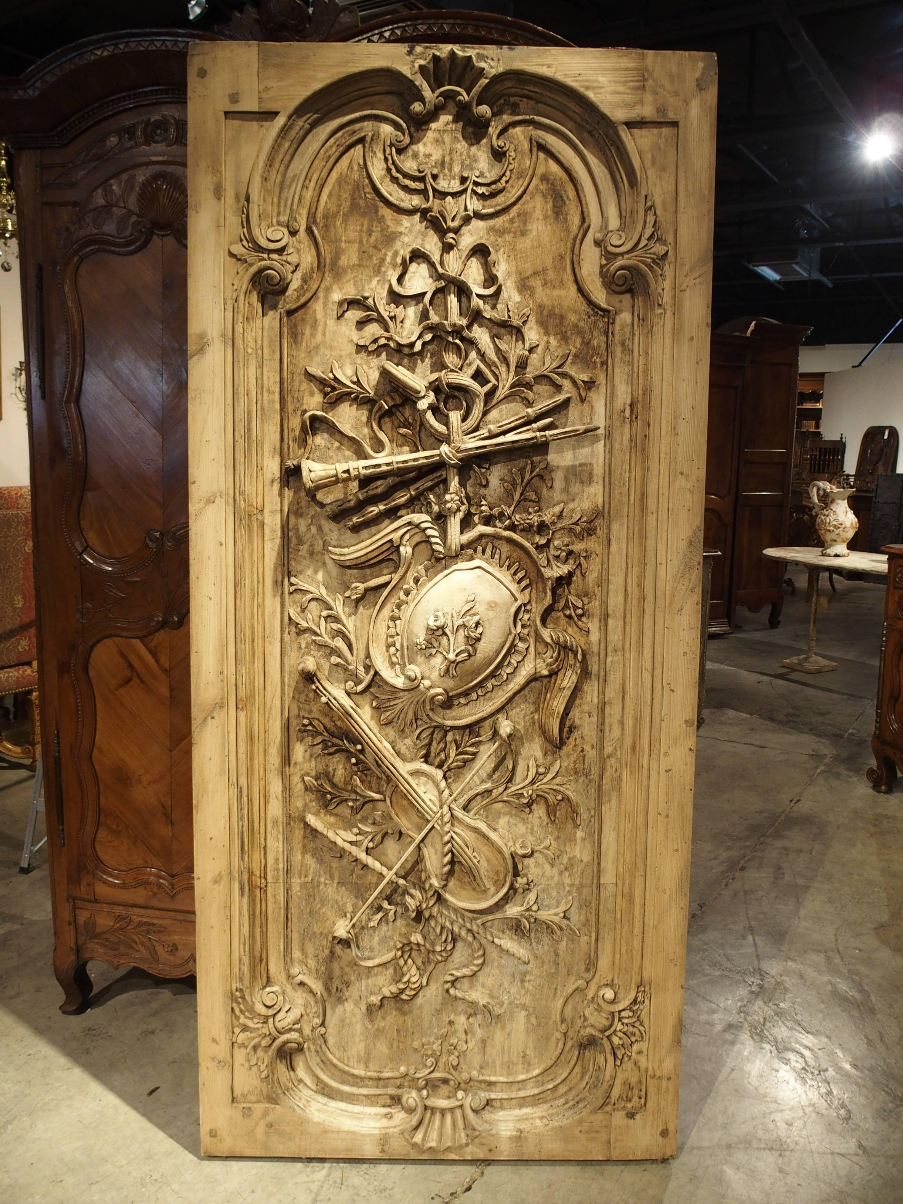 This stunning French interior panel or door, has hand-carved Louis XVI musical trophy ornamentation depicting violins and wind instruments hanging from ribbons and bows. It was created sometime in the 1900s, and the back of the door panel has shaped