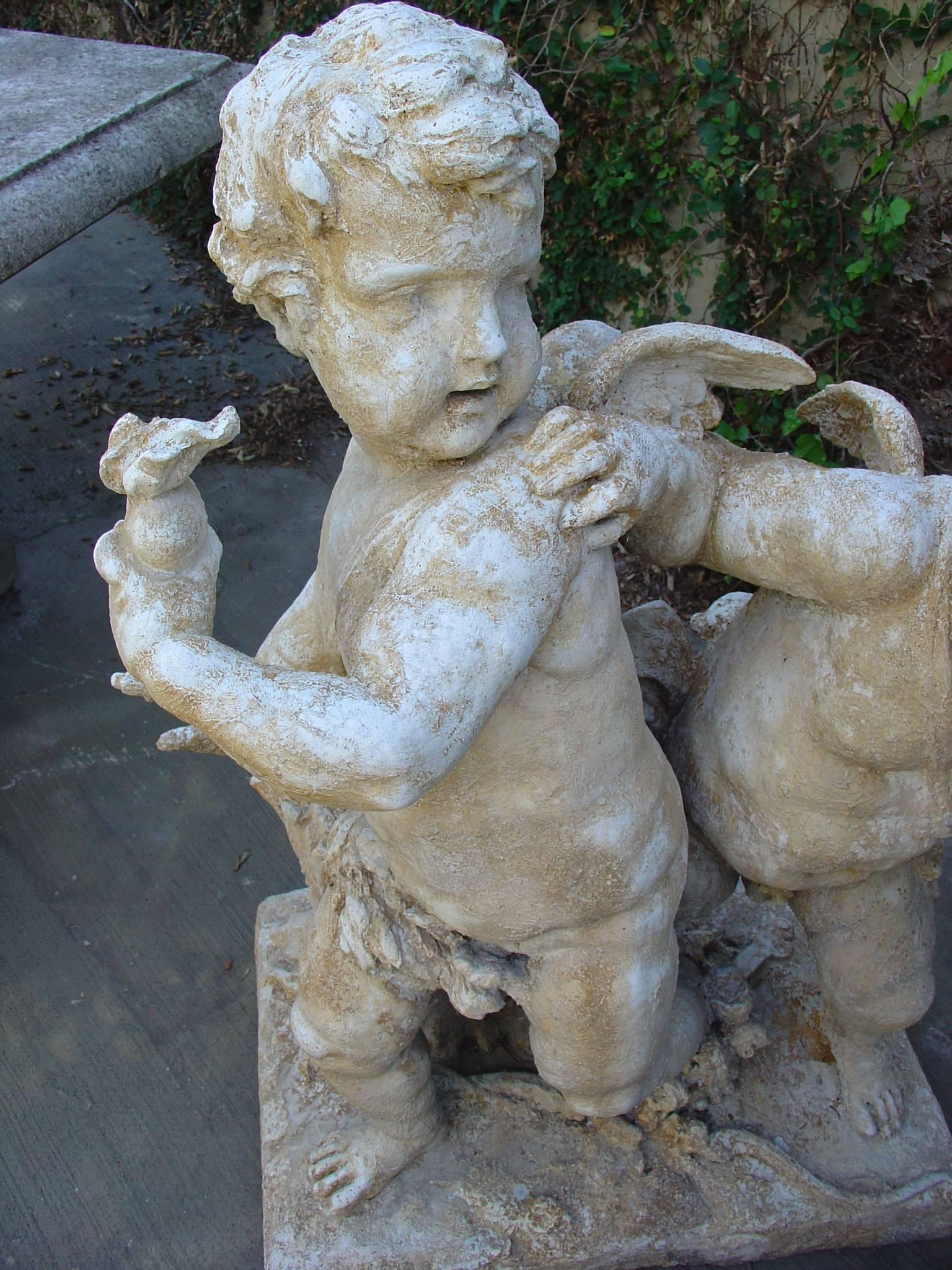 This is a pair of cast stone cupids from France. They are cast from a mold that was taken off the original statue in Paris, France. It was salvaged from a building pediment and was sold to a private collector. First appearing in Classical Greek
