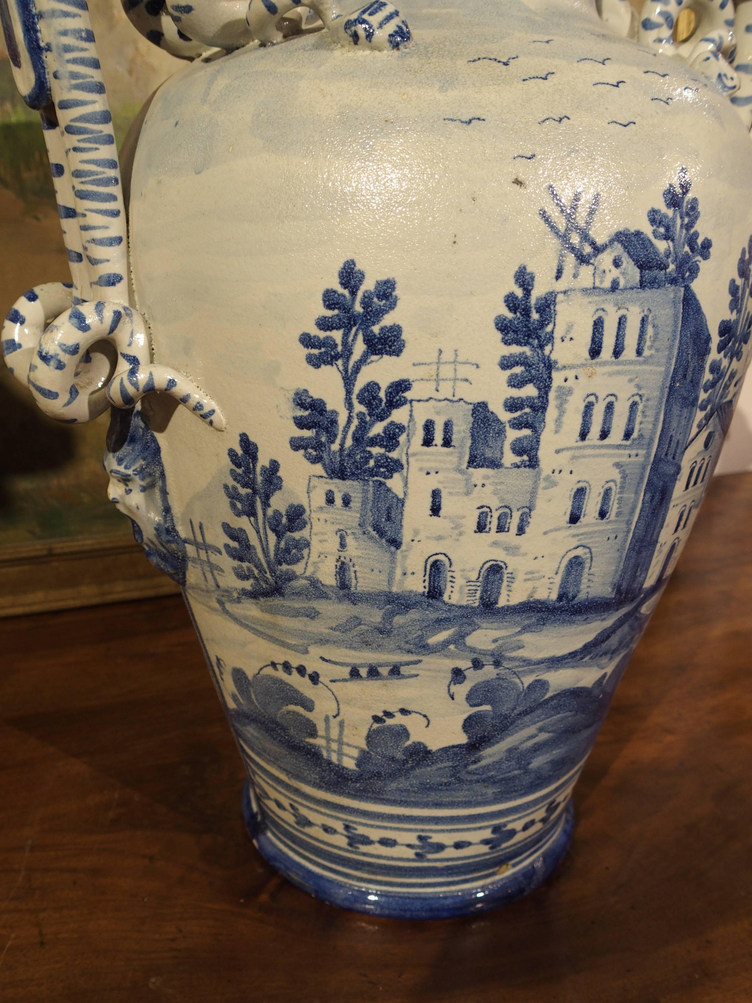 This antique Savona urn has a depiction of a large mythological castle with a smaller one behind it on a landscaped surround. A flock of birds is flying overhead. The reverse side is a large stylized version of a family’s mark (lighthouse) for their