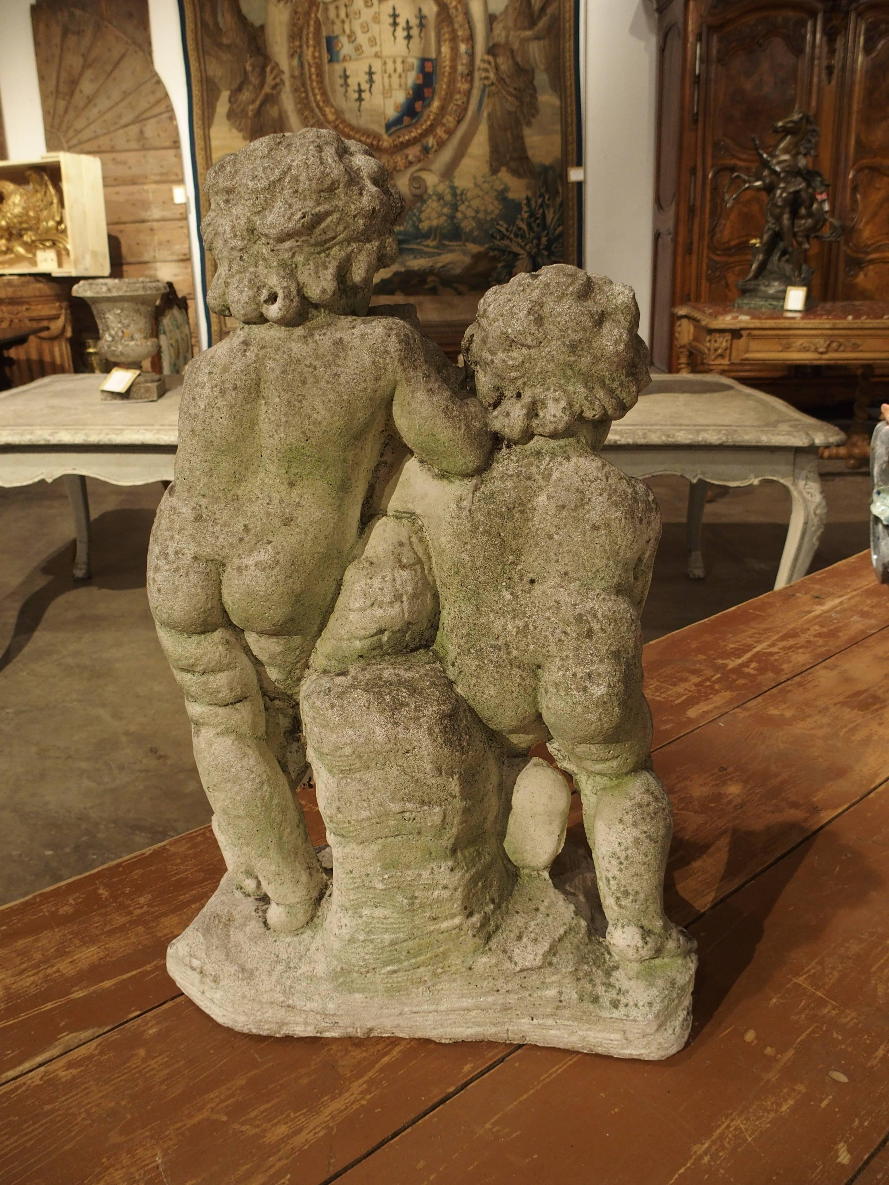 This is a charming antique French stone statue/fountain of two putti and a dolphin. The putto in front is hugging the neck of the dolphin, while the putto to the back is playing a flute. A hole has been drilled in the mouth of the dolphin and comes