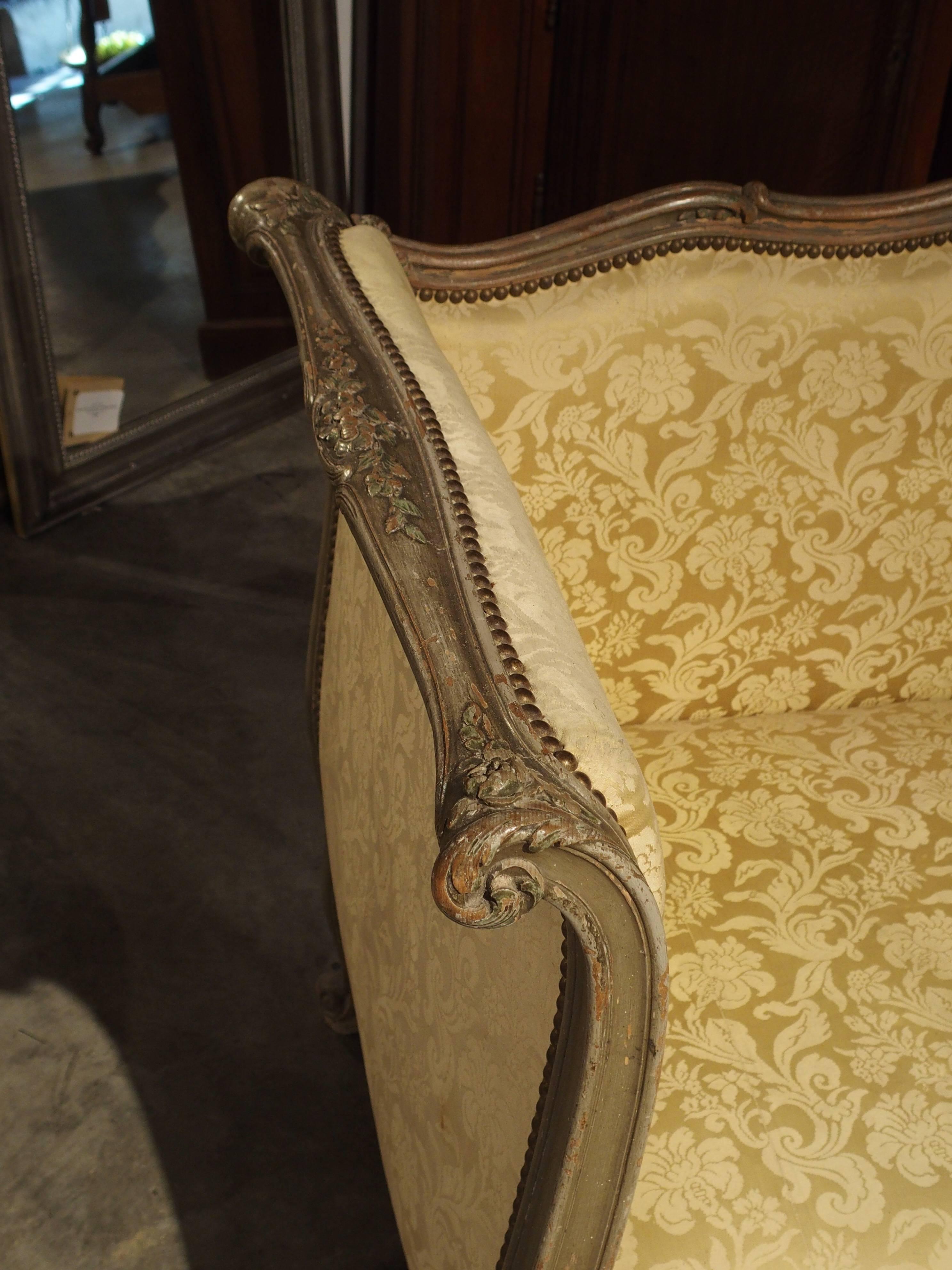 This antique, parcel-paint Louis XV style canapé or settee has a graceful, central domed, shaped back. The scrolled side arms are full height allowing the person to rest their back with full support, if choosing to lounge on the settee. There are