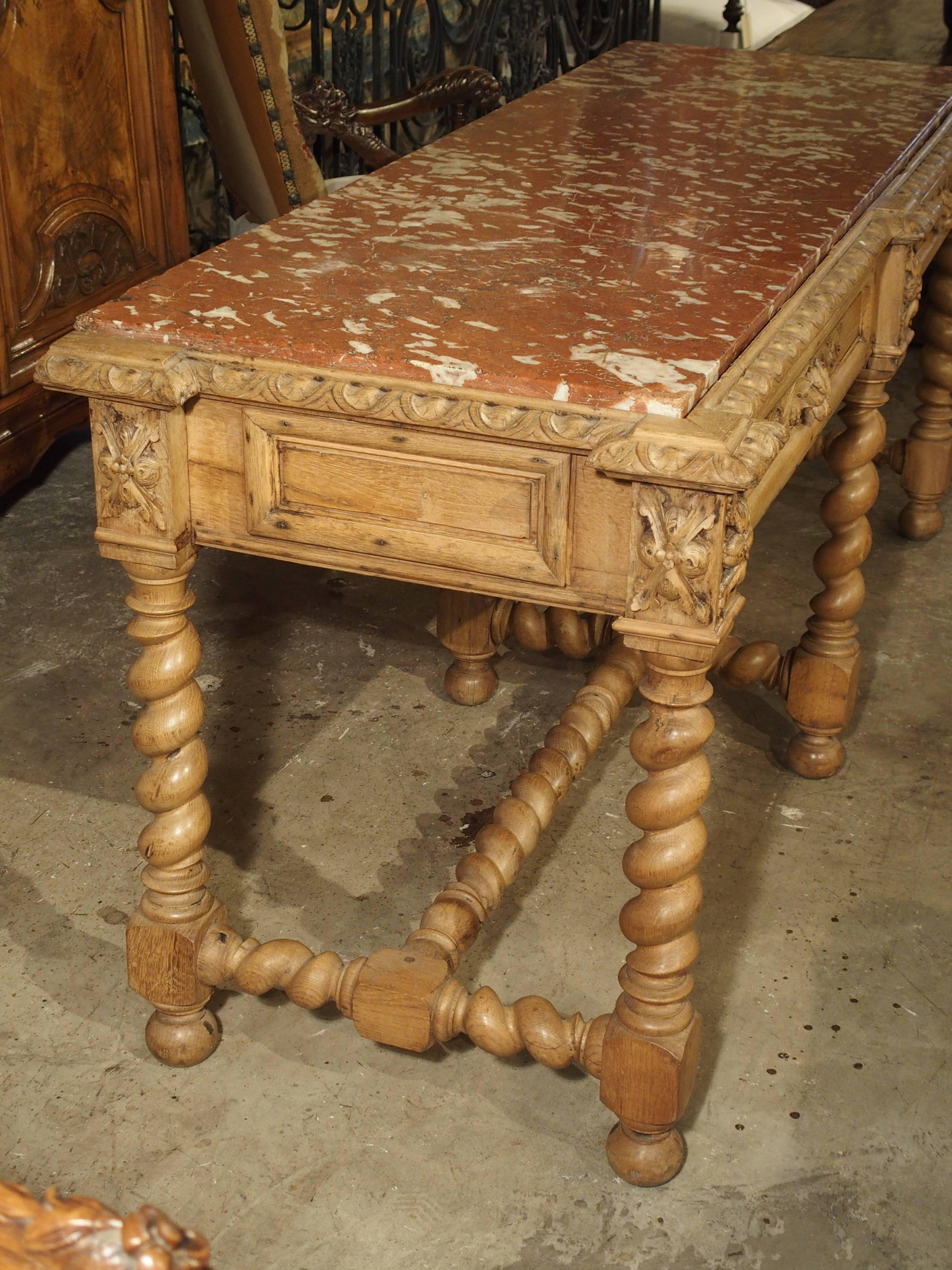 This antique French marble-topped console is in the Louis III style. The European oak has always been natural in its color with a light sealer on it. The rouge Languedoc marble top is inset and surrounded by moldings of gadrooned lunettes, which are