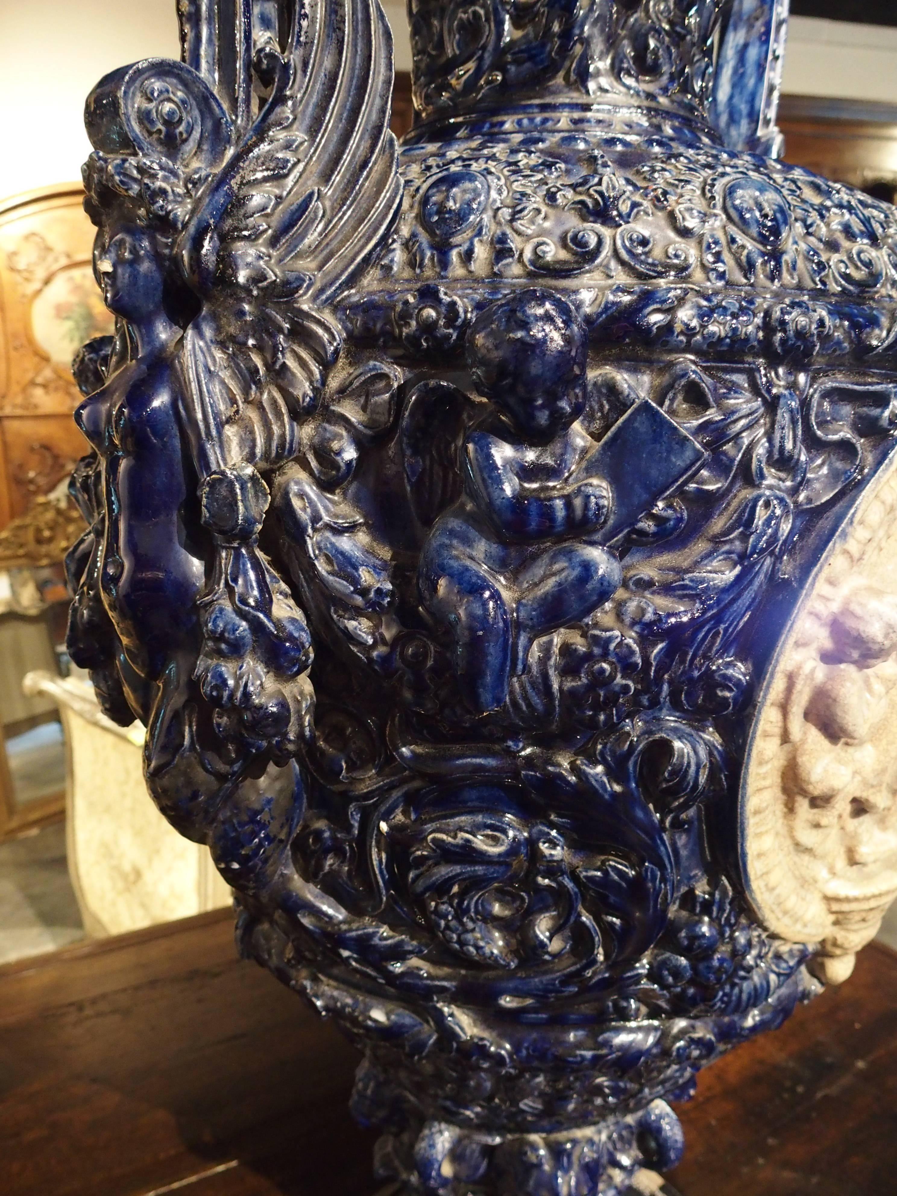 This magnificent antique French, neoclassical style urn is a deep, glossy, cobalt blue and beige and measures over 38 inches tall! It has two scrolling arms decorated with multiple motifs. On either side of the urn are two beige medallions depicting