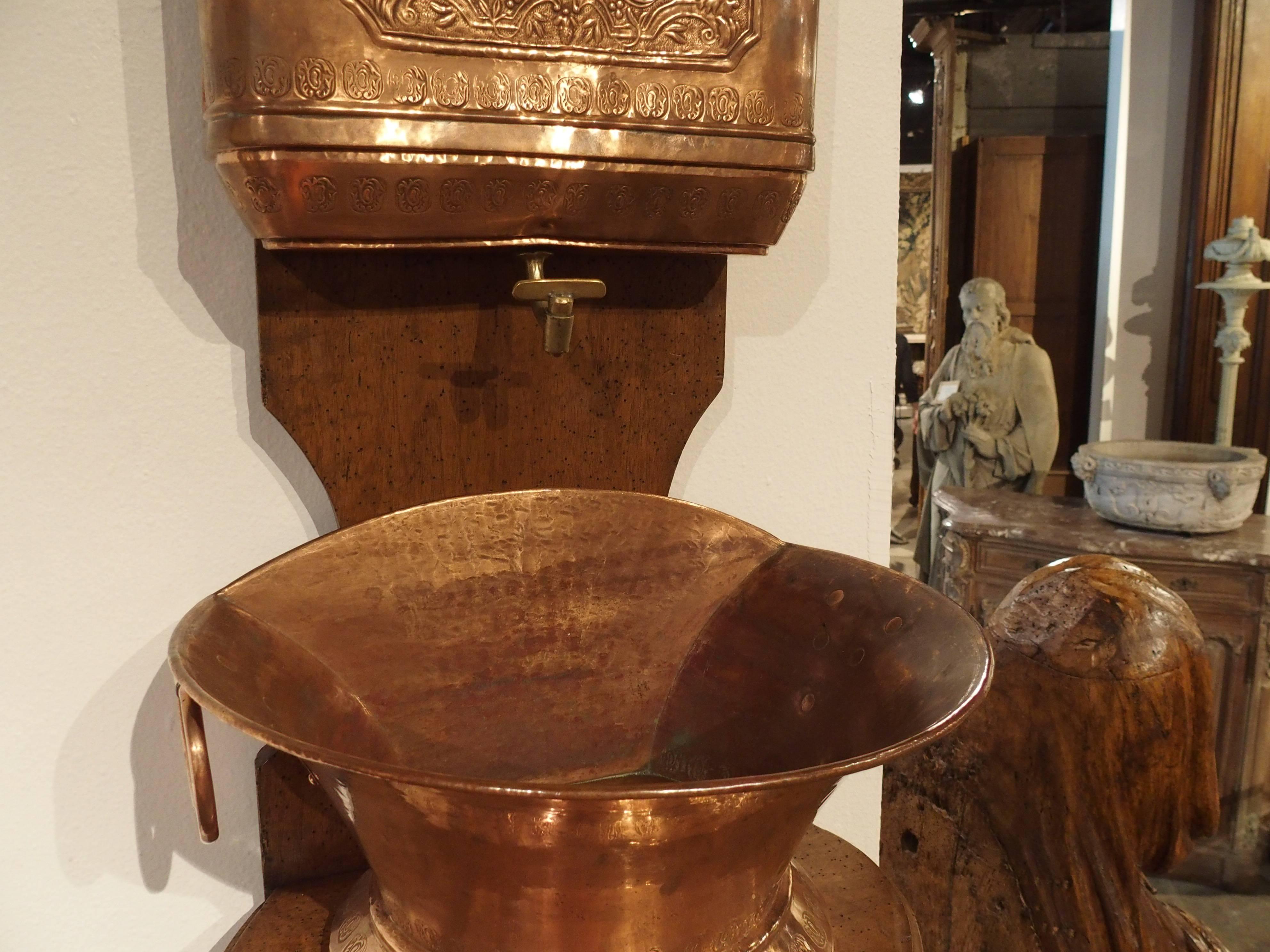 This 19th century French repousse copper lavabo on an original walnut wood Stand has a coat of arms on the front of the upper storage tank where the water is held. A bronze spigot would have allowed the water to empty into the bottom basin by