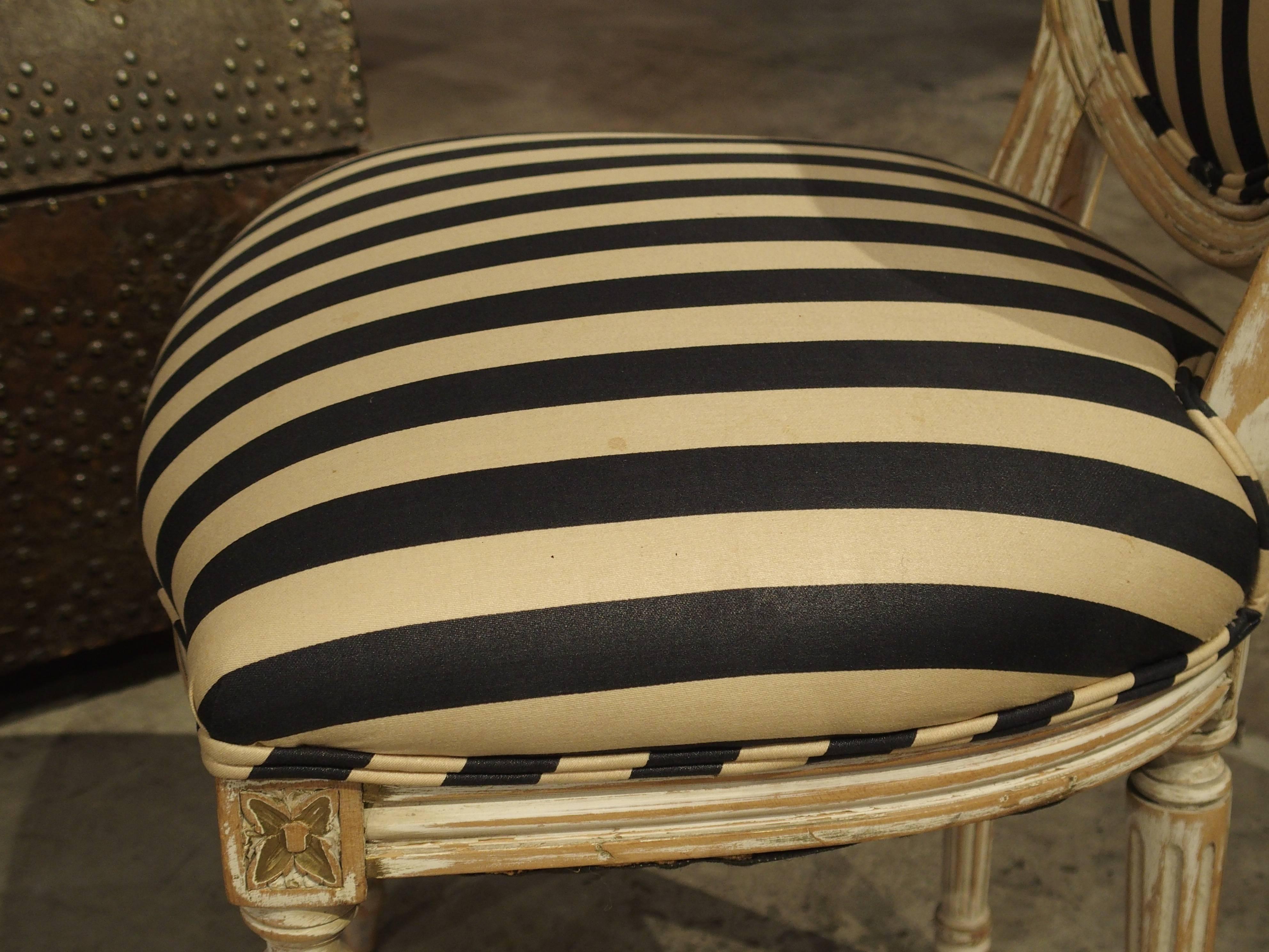 This charming pair of antique French Louis XVI side chairs have medallion curved backs and a parcel painted finish. At one point in their history, they were gilded or painted and were later stripped.  The vertical stripe upholstery has been recently