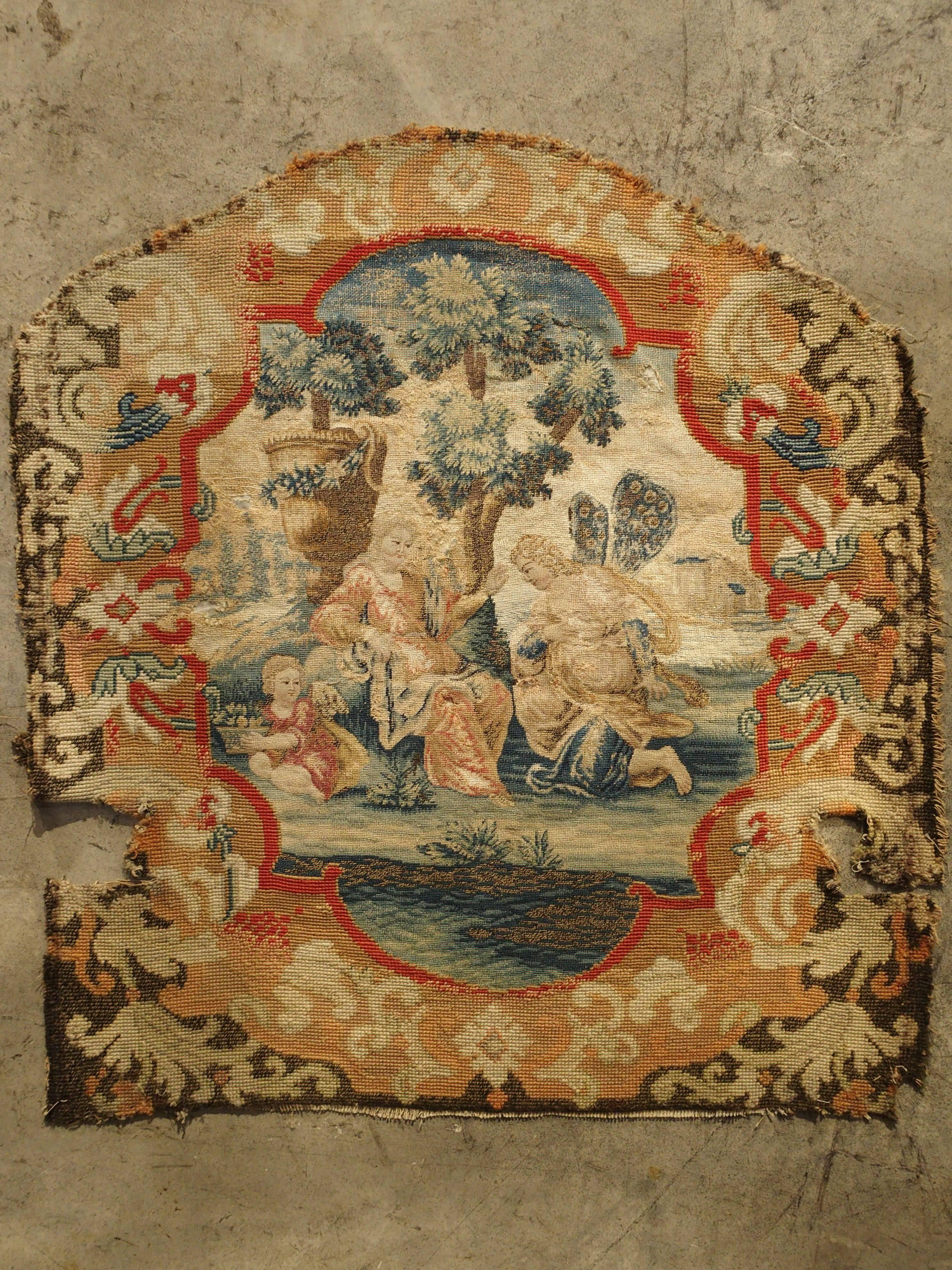 This magnificent 17th century French tapestry chair back panel with needlepoint border has most likely outlived the original wooden frame it was made for.  The central scene depicts a garden setting with a body of water, a large medici urn, and