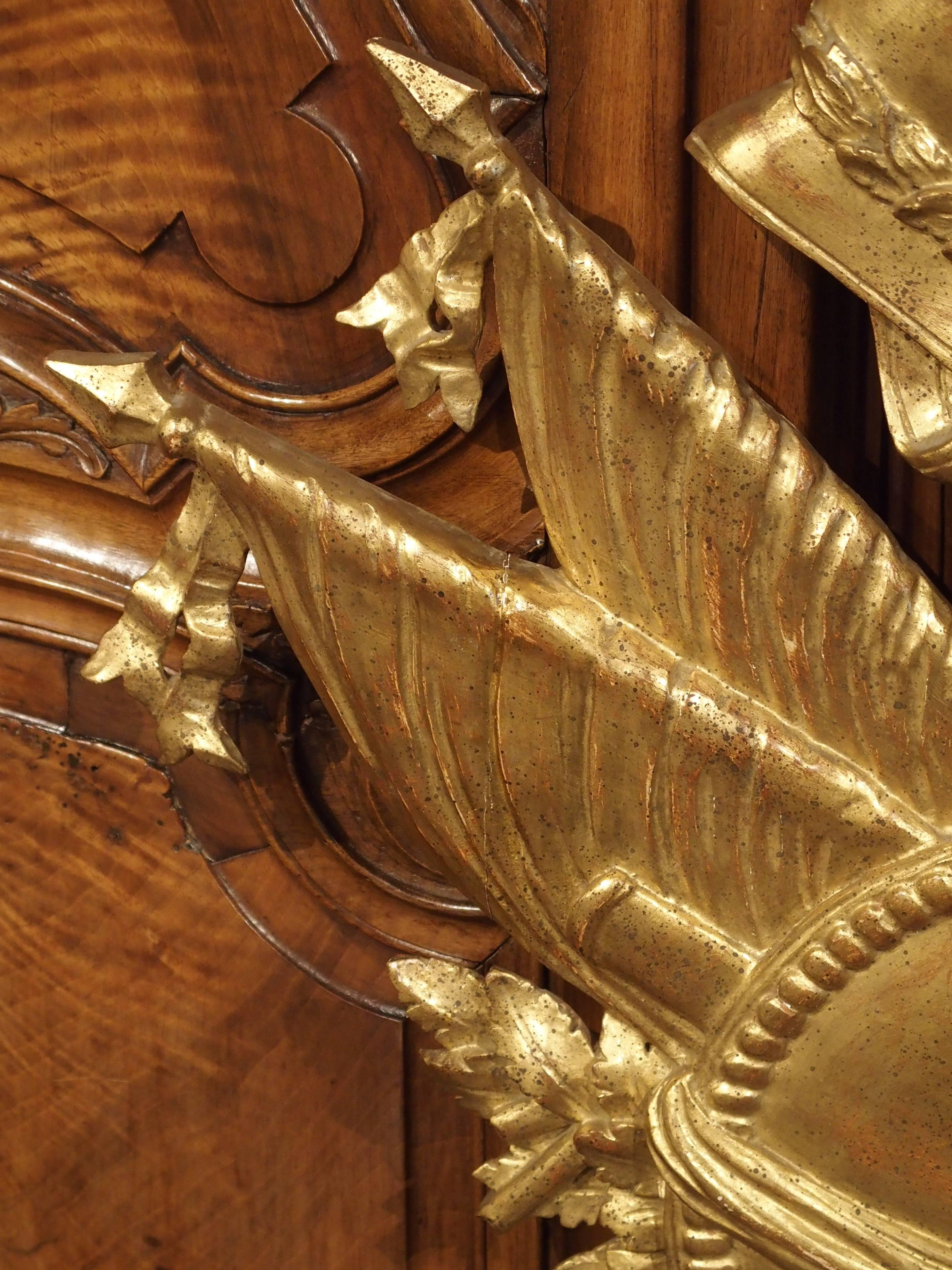 This stunning giltwood piece is known as a military trophy. It is carved and gilded wood and made in Italy, in the 1900s. This type of piece would have been intended for decorating a wall, an overmantel, or even an overdoor. The depiction of
