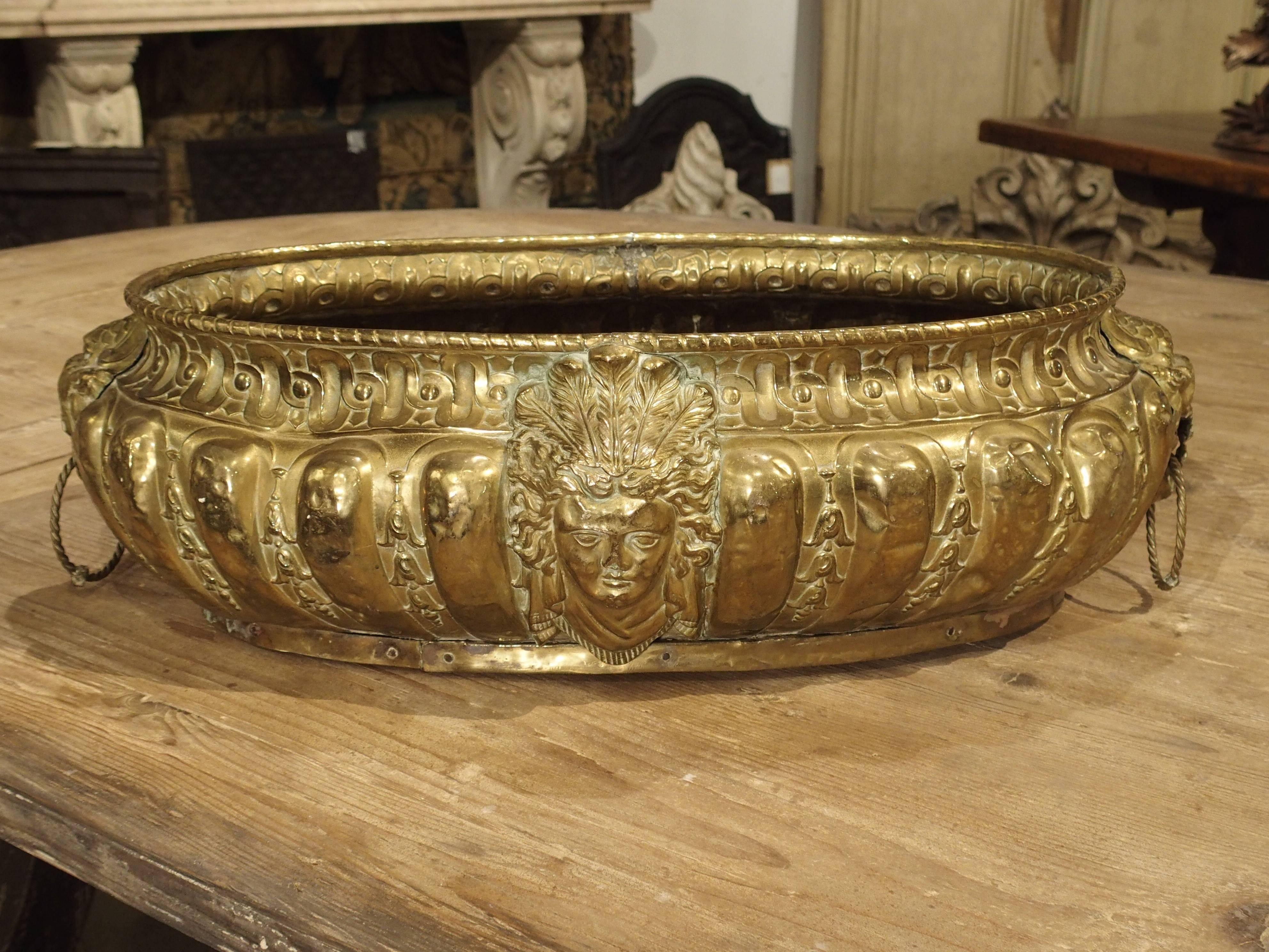 This is a large, oval form repousse (relief) brass planter with a wood bottom and two handles. All of the relief work was hand-hammered and it is fully decorated on all sides. This piece dates to the mid to late 19th century and originates from