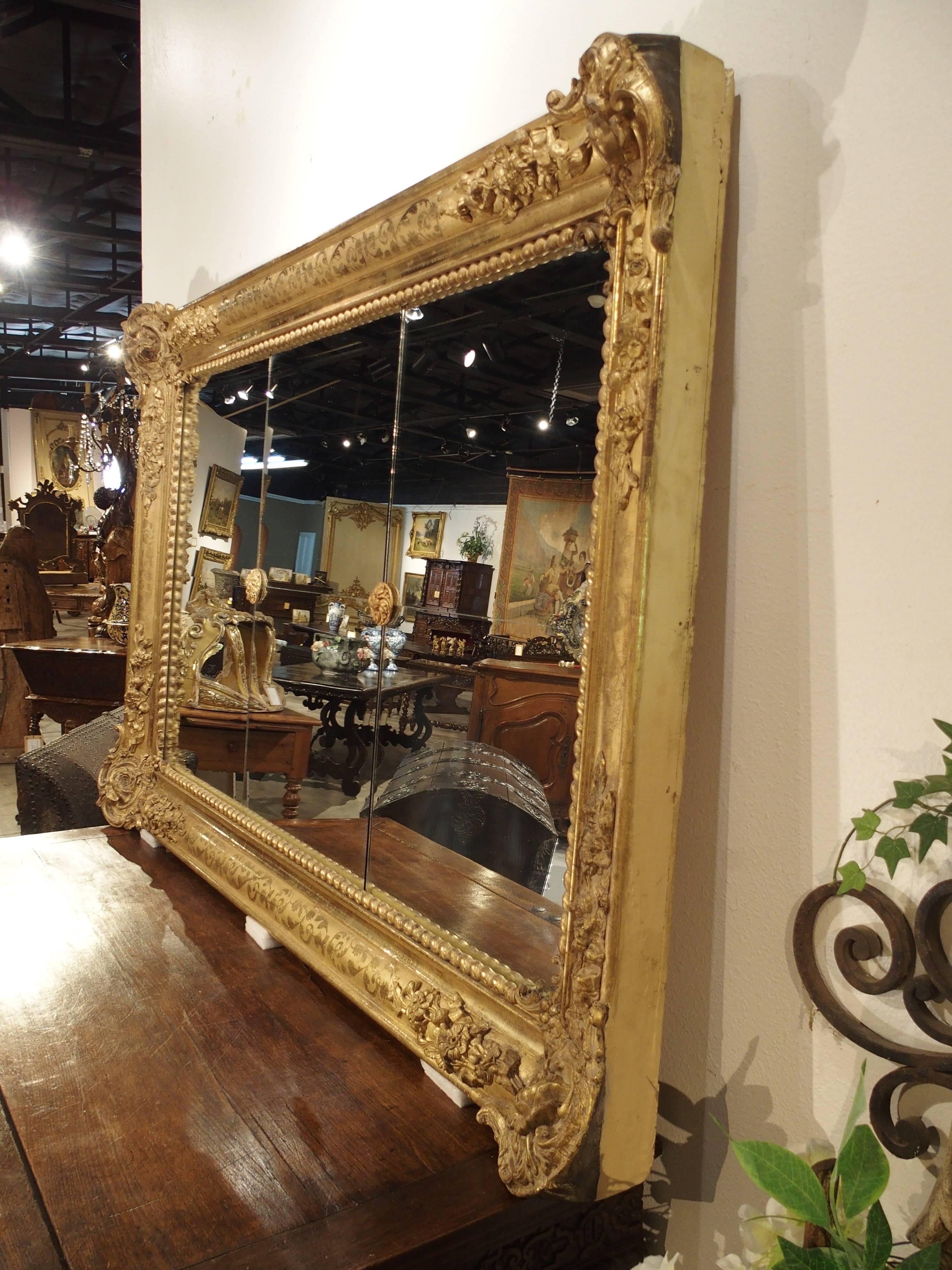 This elegant antique French, giltwood, rectangular mirror has absolutely stunning ornamentation. At the corners are motifs of roses with trailing vines, various flowers and ribbons to either side. On the mouldings are incised, scrolling floral and