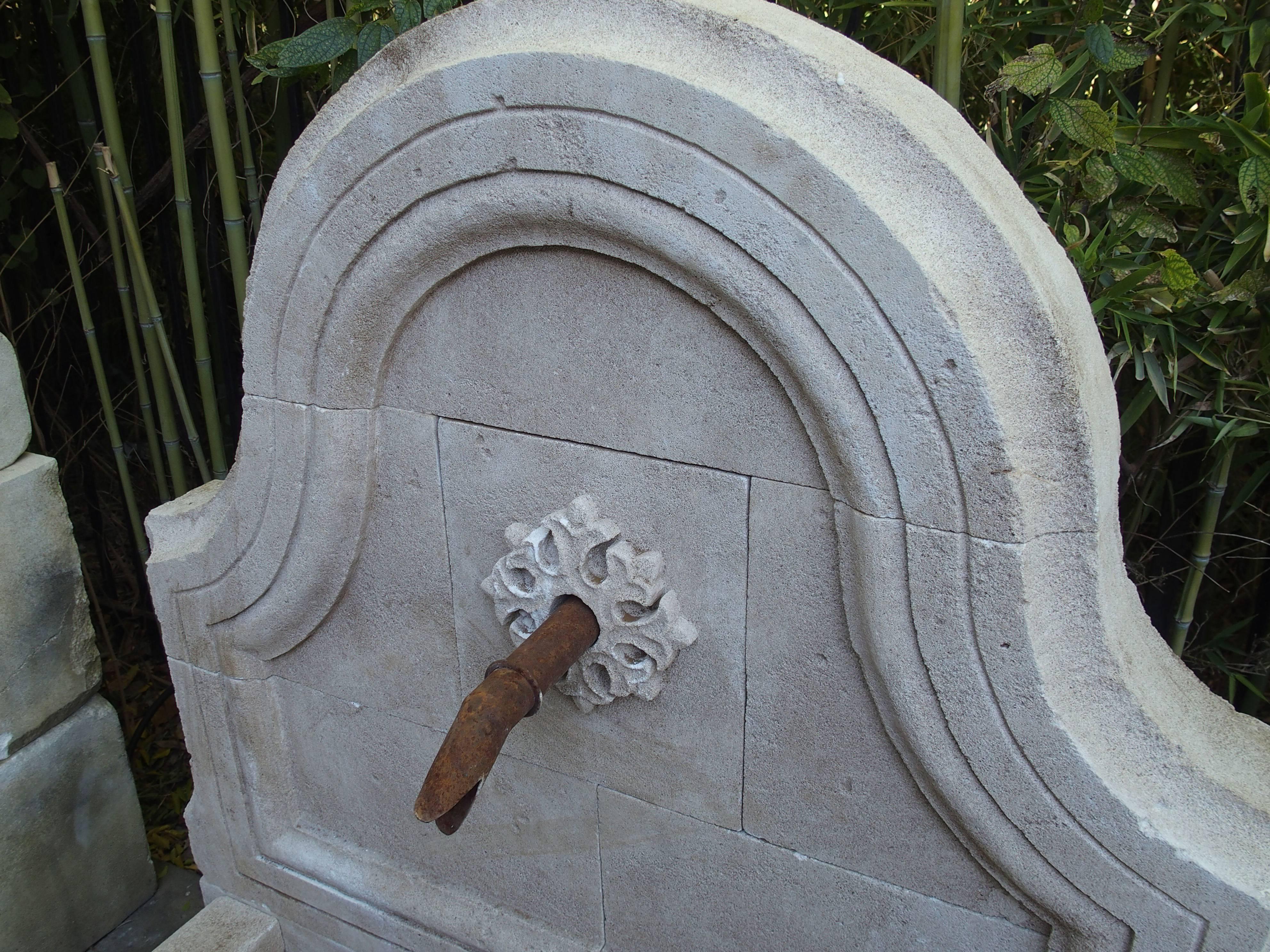 This small French wall fountain has been hand-carved and distressed out of solid French limestone. The back of the fountain has a unique, arched center panel with shaped moldings and incised frontal ornamentation. There is a rusted spout surrounded