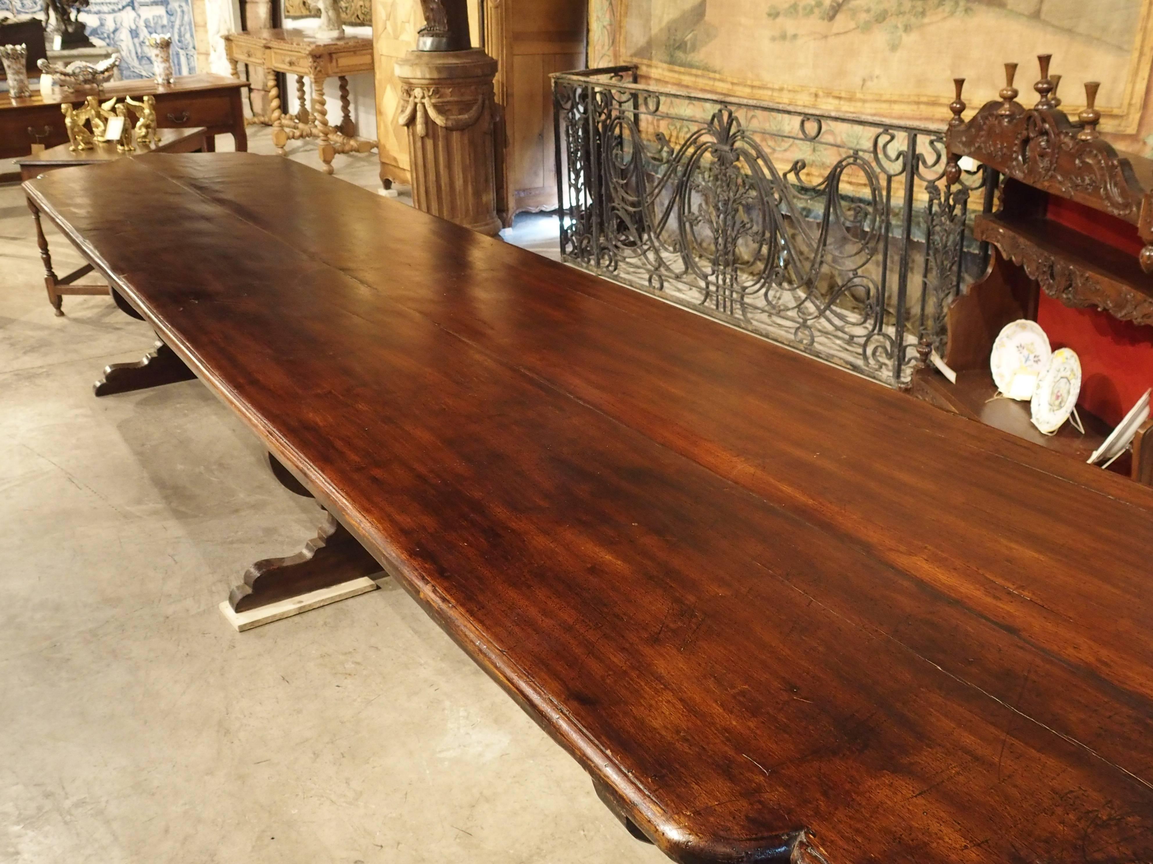 This extremely long, Italian table with thick, curved, iron stretchers is absolutely magnificent! It is a little over fifteen feet long and has been made from Italian walnut wood. At either end of the tabletop, there is a central arch with shaped