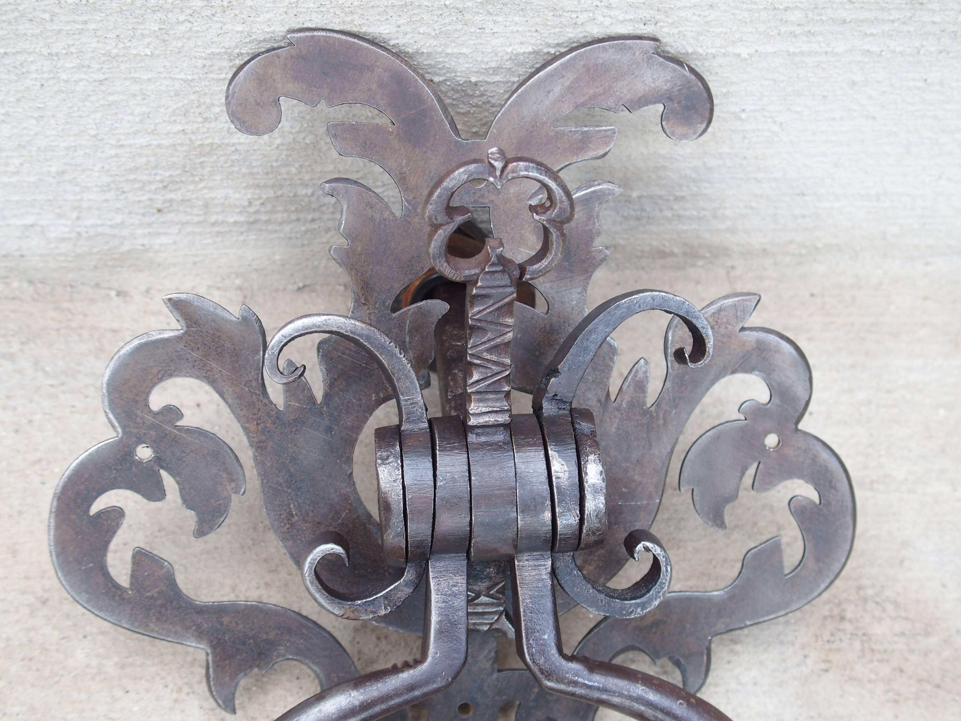 This 18th century French door knocker has a unique design with a central vertical key motif. It has a pierced scrolled top with a shaft that has incised dog tooth motifs on it. C-scrolls are on either side. Beneath all this is the knocker handle