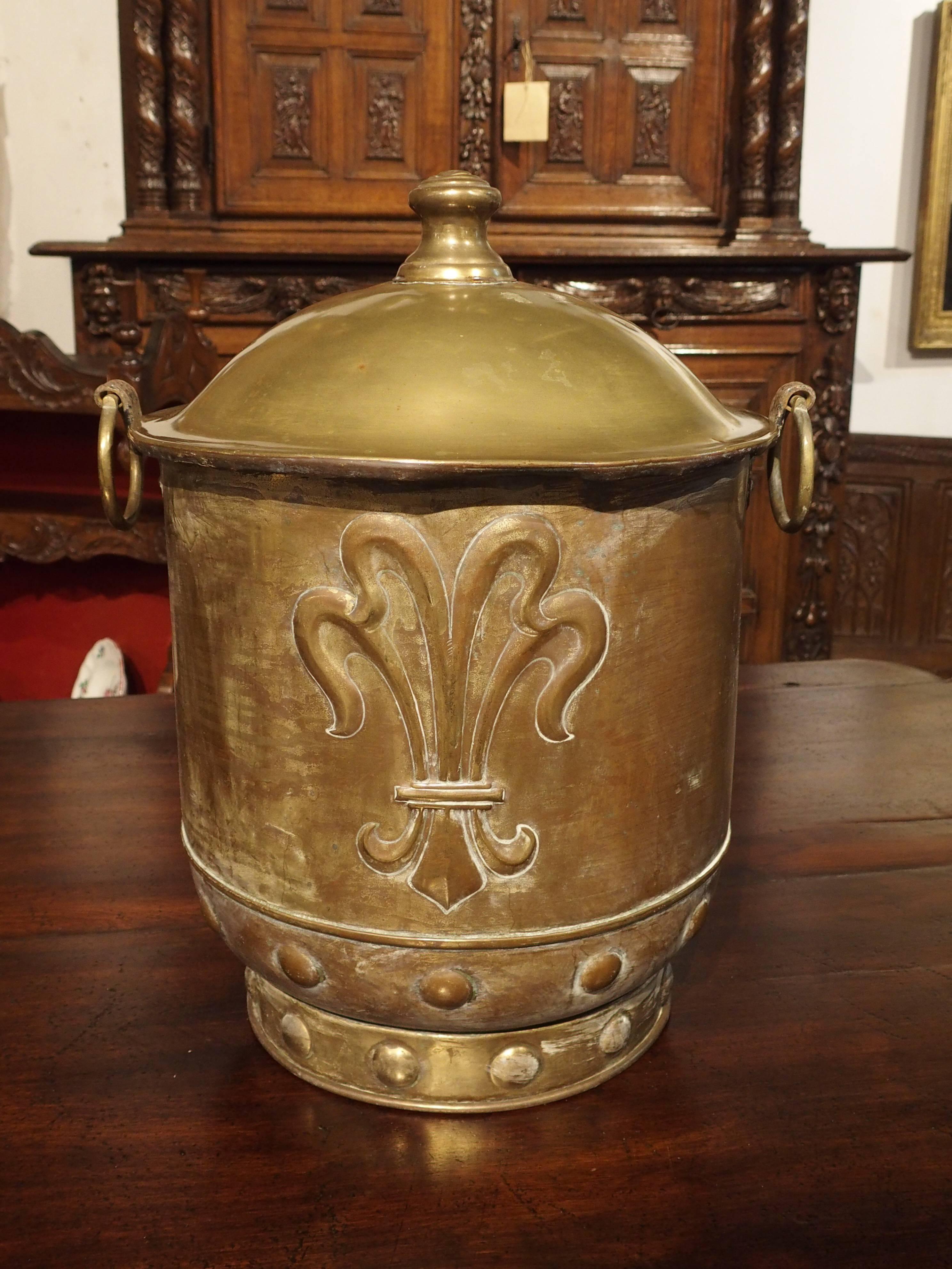 This wonderful large brass container from France has motifs of a repousse helmeted shield surrounded by scrolling acanthus leaves. Three crown motifs are on the shield. The other side of the container has a large repousse Fleur de Lis. At the bottom