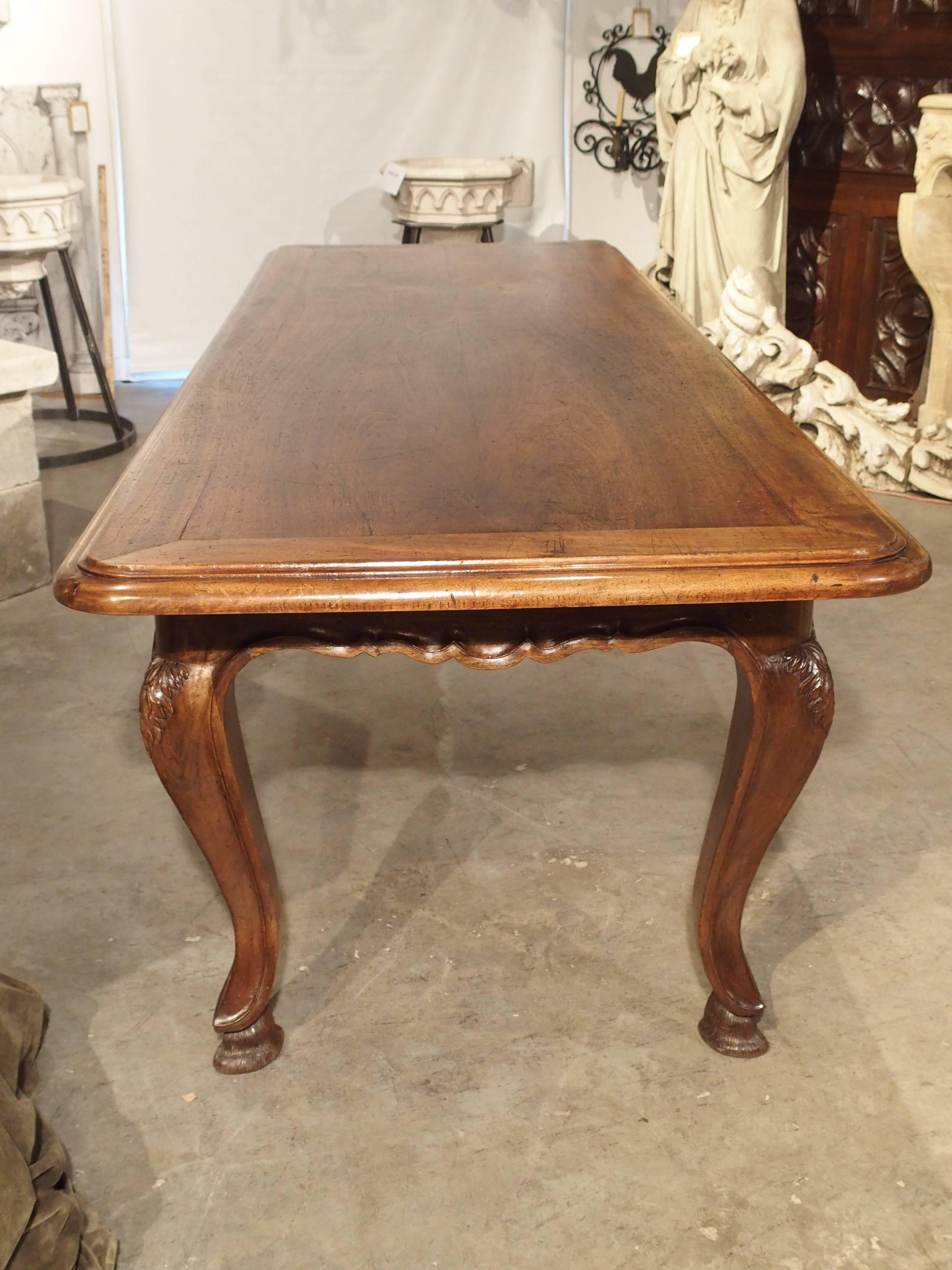 This stunning and very long, Louis XV Style, walnut wood table has been superbly crafted. The top has stepped out layers of wood, one indented layer over a thicker bullnose layer. The beautifully scalloped apron surrounds all four sides and is