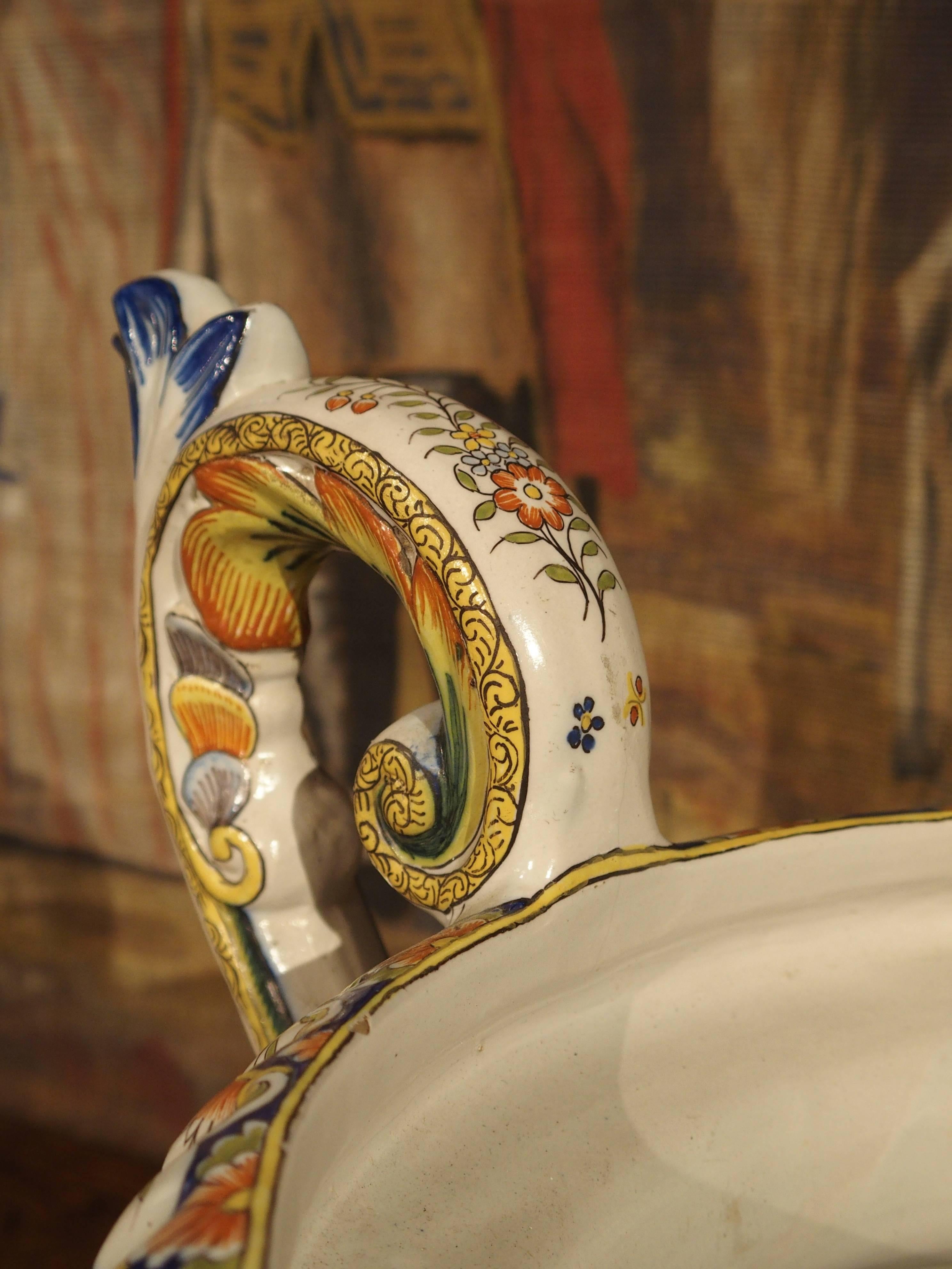 This antique French faience urn has been hand-painted with very fine detail in all of its motifs. It is from the Desvres region of France. The rim has a cobalt blue ground with white insets. Orange, yellow and light olive green flowers and foliage