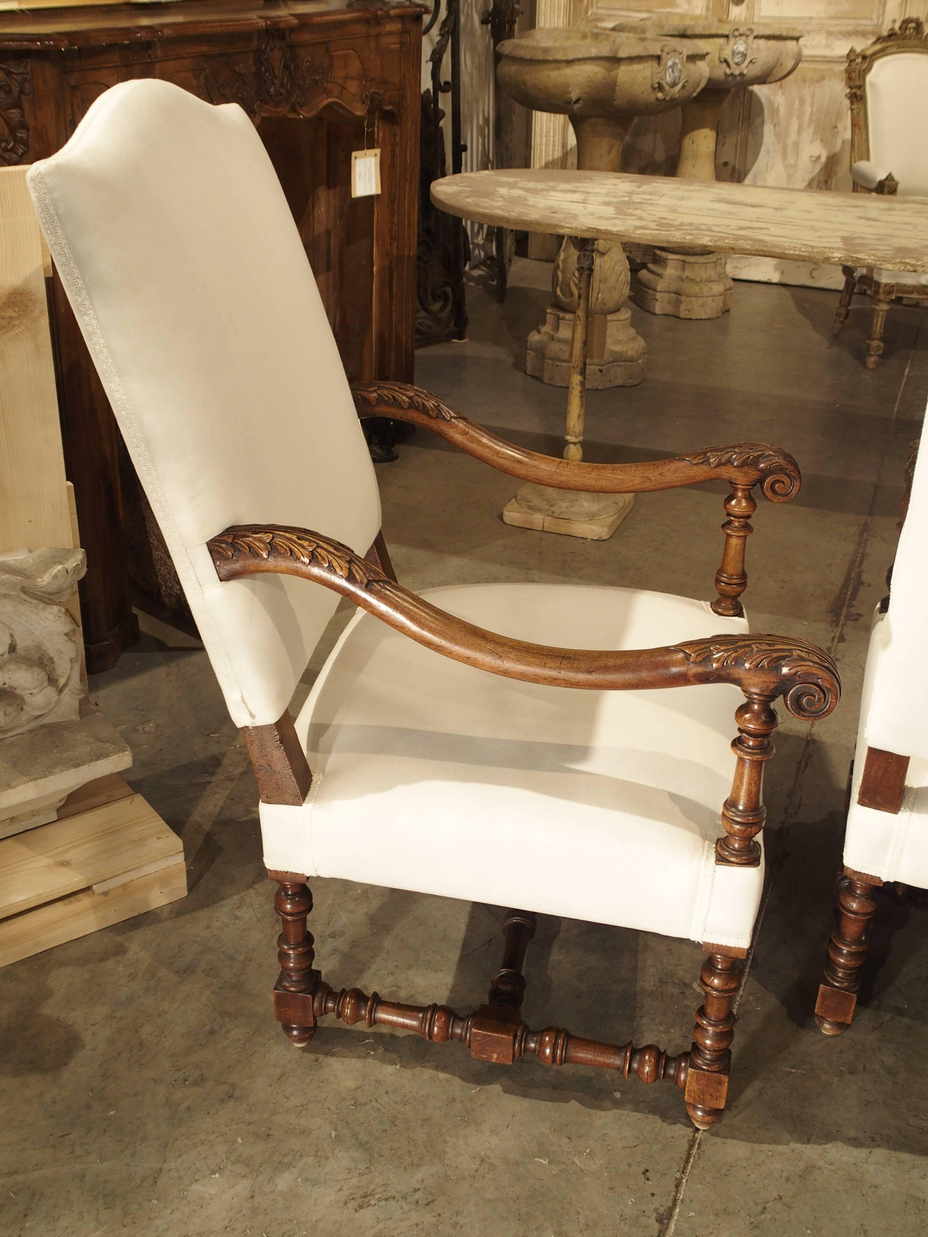 This wonderful pair of antique French, walnut wood armchairs has been covered in muslin with gimp trim. The arms are carved with acanthus leaf motifs with baluster terminals. The terminals line up with the legs which are baluster turned and the