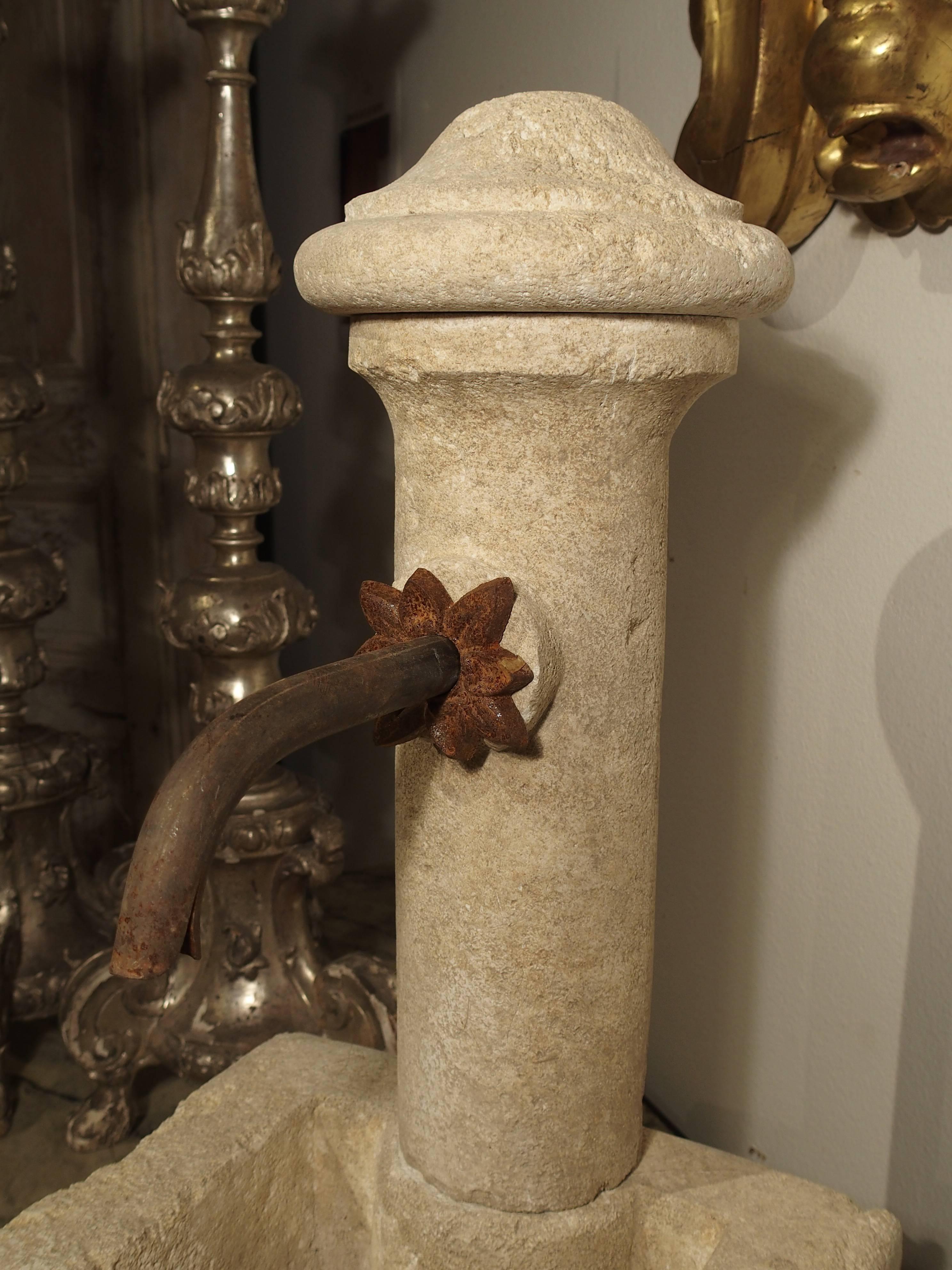 This unusual and charming French tabletop or small garden fountain has been hand-carved in Provence, from Estaillade stone. The fountain has a round columnar back where the spout is. A decorative iron foliate motif surrounds the opening for the