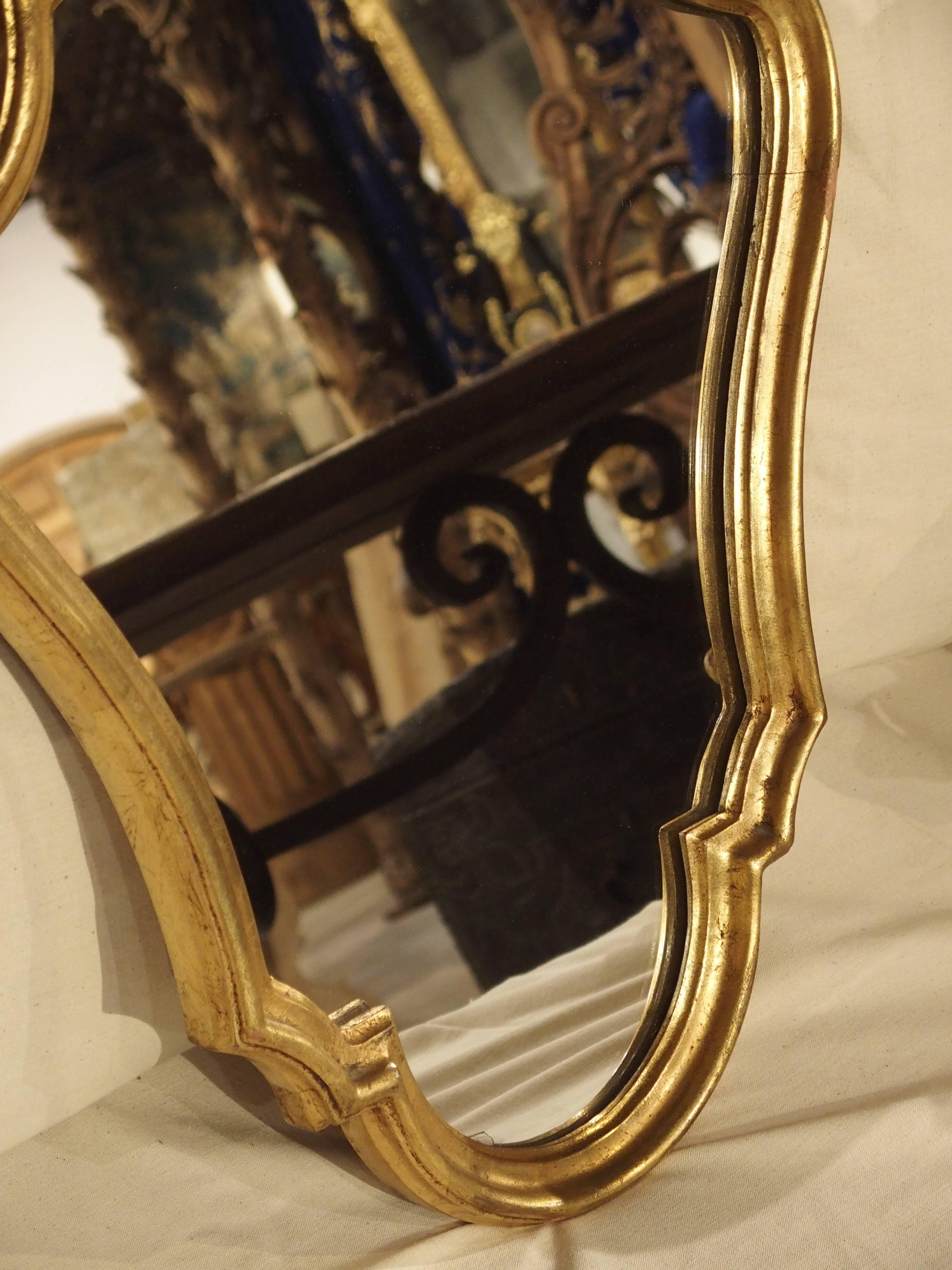 This vintage, shaped, giltwood mirror from France has interesting lines throughout. Right angles are paired with curves and the shape is trapezoidal with the narrow part at the bottom. With only one motif of a shell and foliage at the top, this