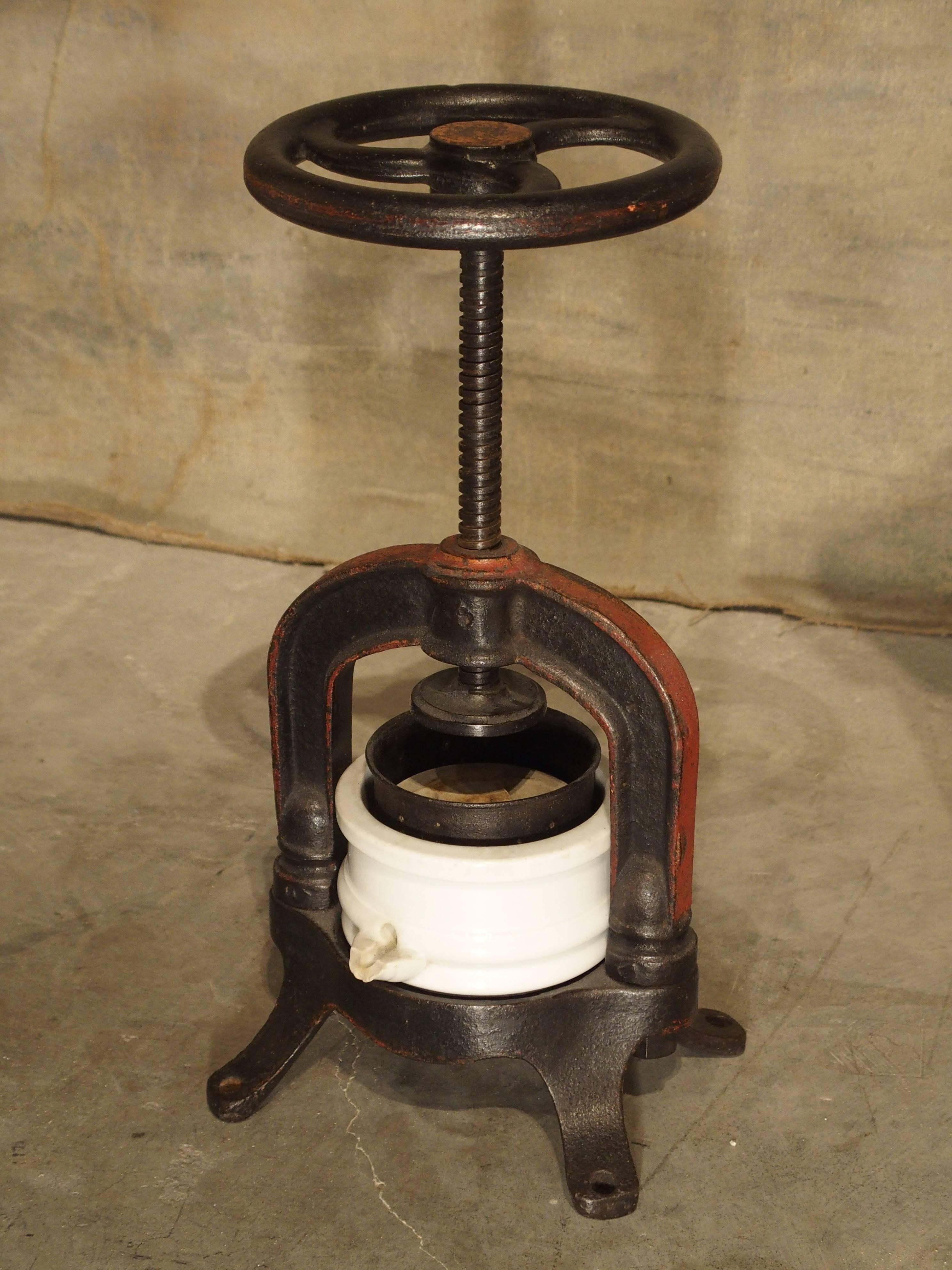 This small press dates to the beginning of the 1900s, but they first appeared in the 1800s. It is made of cast iron (partial old paint remains), a ceramic juice container and its original strainer. Each leg would have been bolted to a table to keep