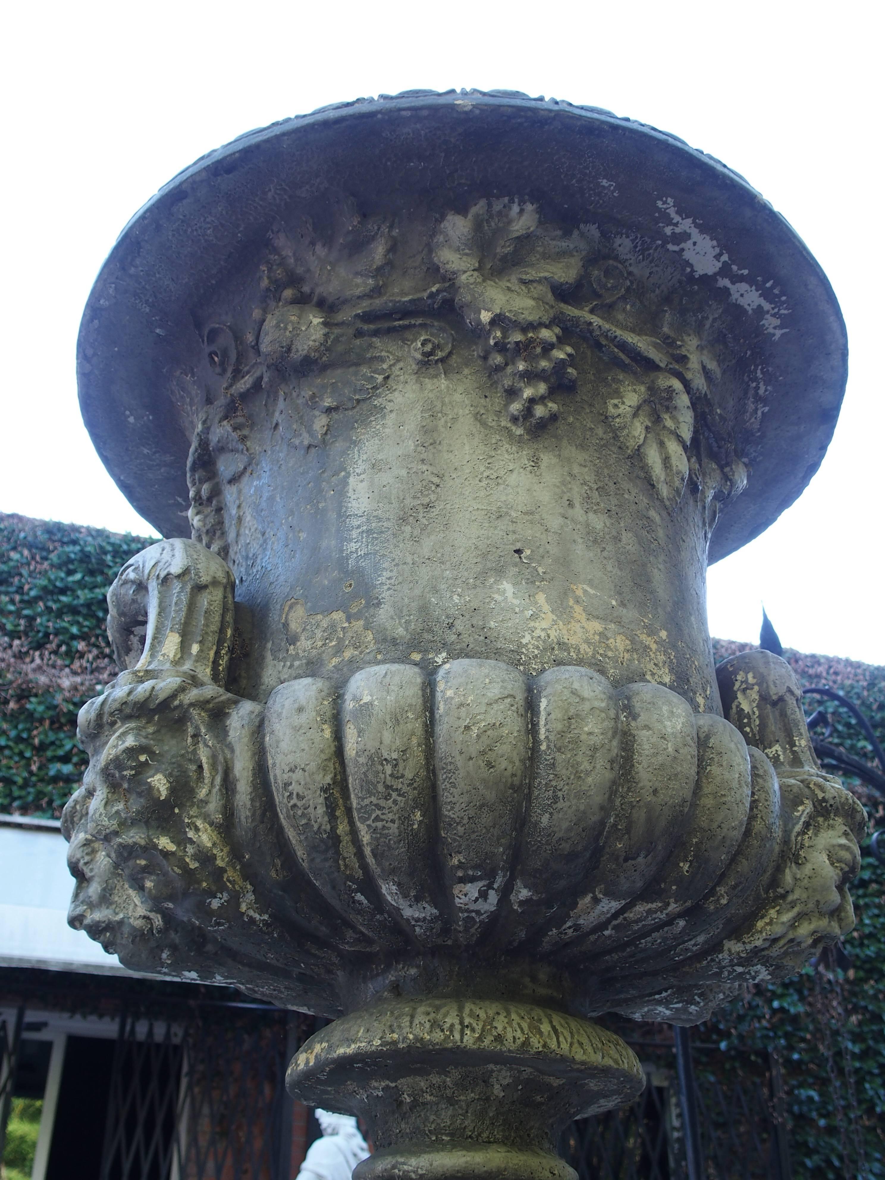 These urns on pedestals are based on the Medici vase of antiquity. These were made in France with similar double handles in the shape of stylized dolphins rising from satyrs heads on either side of the urns. The frieze has motifs of flowing grape