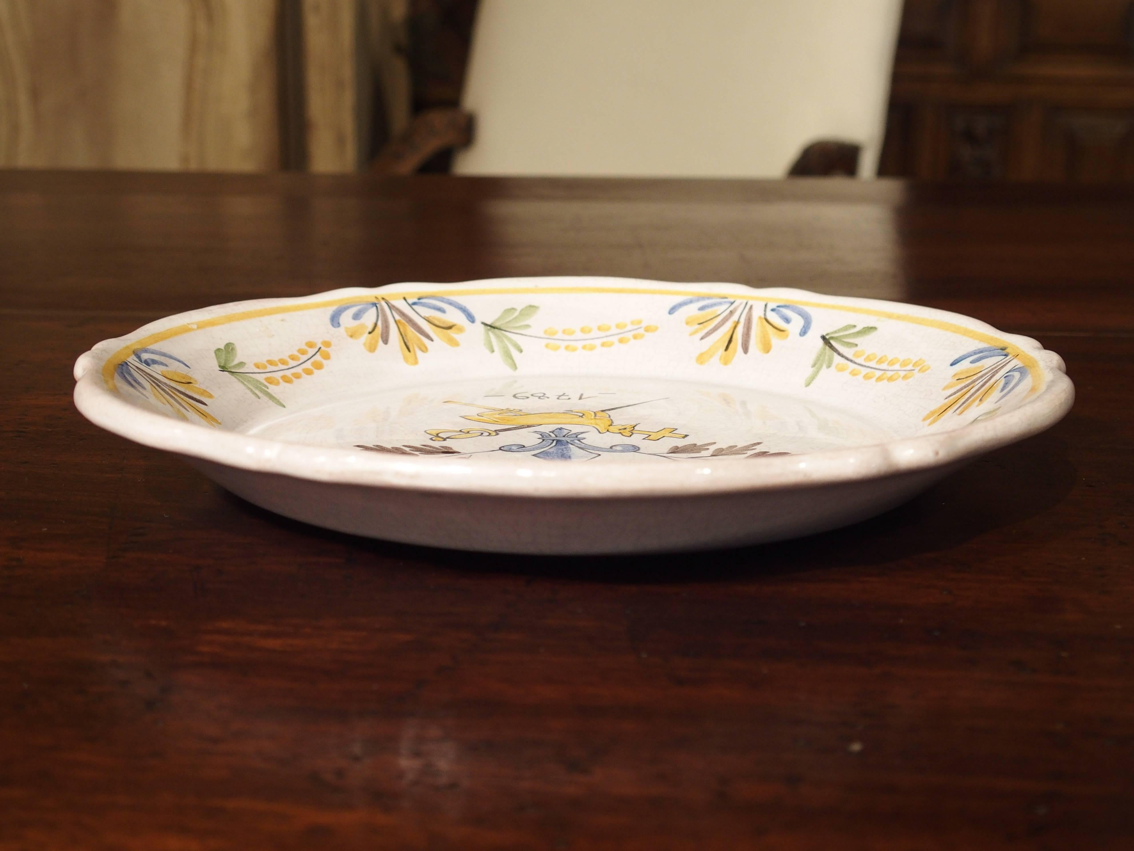 This reproduction French plate is after an original 18th century French Faience plate. It has a crown over a fleur-de-lis with an animal in front of a sword and cross. A date of 1789 is beneath this. It is hand-painted and very decorative. These