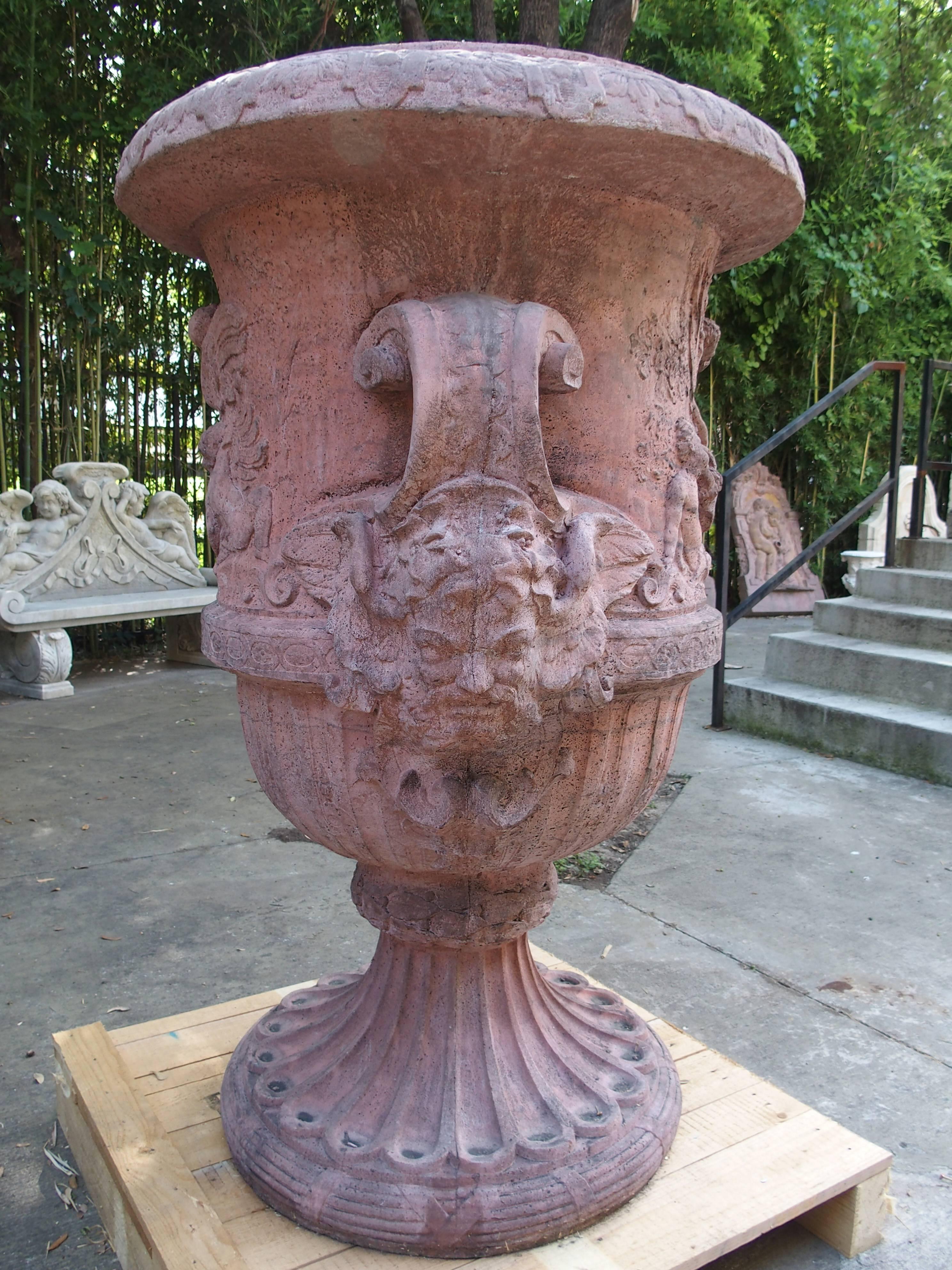 These large, cast stone urns have been made with a mixture of crushed limestone, bluestone, and cement. The terracotta color has been mixed in with the stone, not applied. Their detailed scenes which are in relief, are of mischievous putti at play